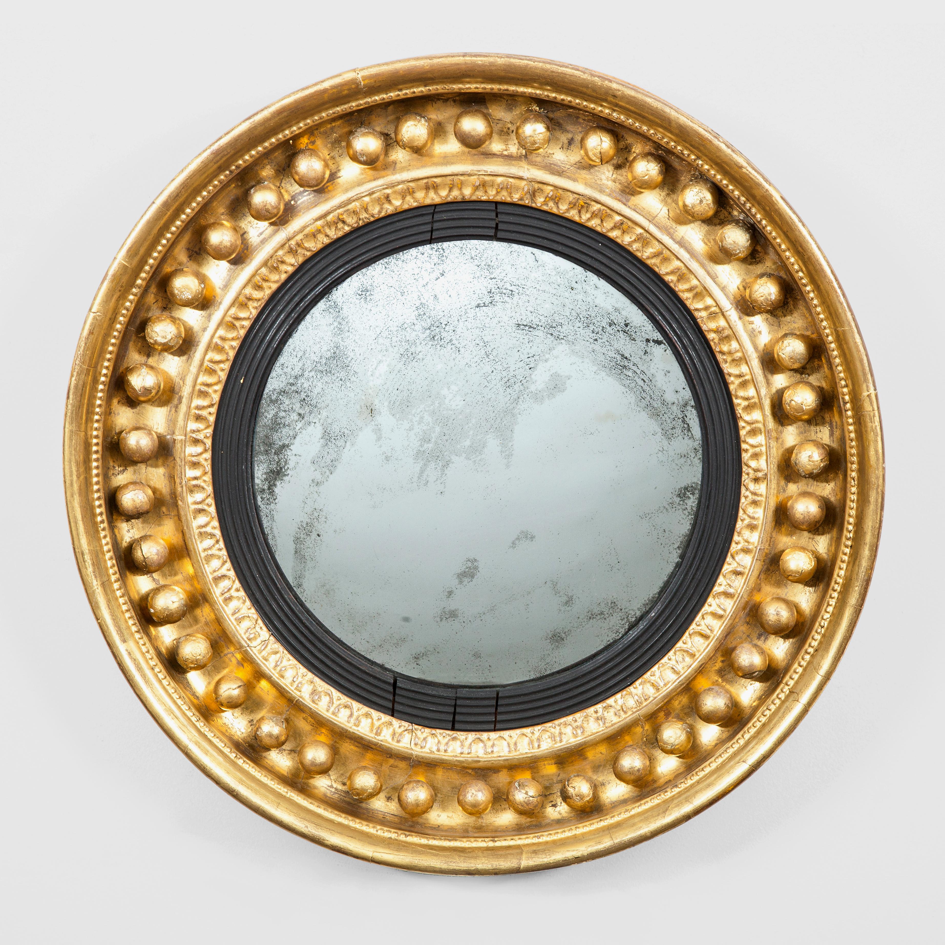 Regency period giltwood convex wall mirror, the circular mirrored plate and reeded slip and egg and dart border set within a deep molded concave frame set with gilded spherules, the outer frame surrounded by a small beaded border.