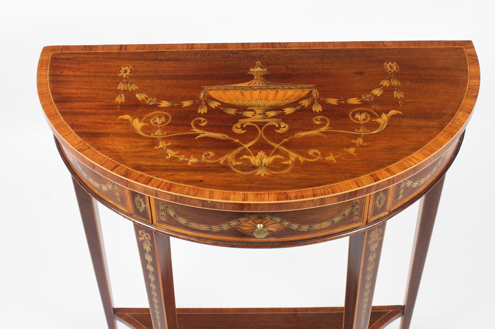 This is a beautiful antique English Regency Revival mahogany and marquetry demilune console table, circa 1900 in-date.

The half-round table top is beautifully framed with a satinwood border and has a finely inlaid marquetry central urn within