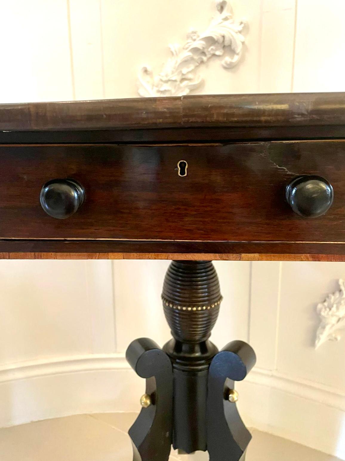 Antique regency rosewood lamp table having a quality rosewood top with satinwood inlay ,one drawer and one dummy draw to the frieze with original turned wooden knobs. It is raised on a charming turned shaped ebonized column standing on three shaped
