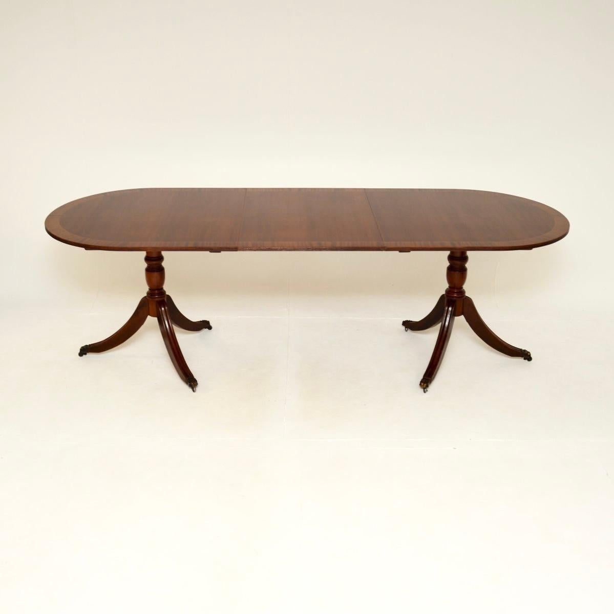 A lovely antique Regency style extending dining table. This was made in England, it dates from around the 1930’s.

It has a beautiful top with cross banded edges in satinwood. Each half sits on a pedestal tripod base with reeded legs and brass hairy