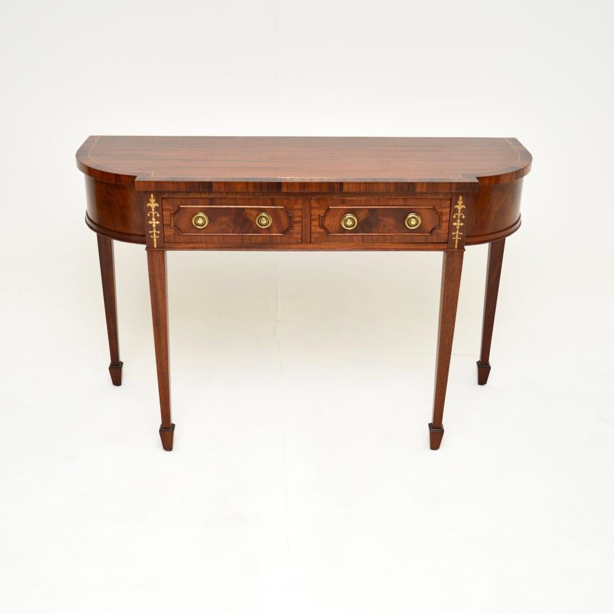 An impressive antique inlaid brass console table. It is in the Regency style, it was made in England and dates from around the 1950’s.

This is of outstanding quality, the mahogany has gorgeous grain patterns and the brass inlays compliment it