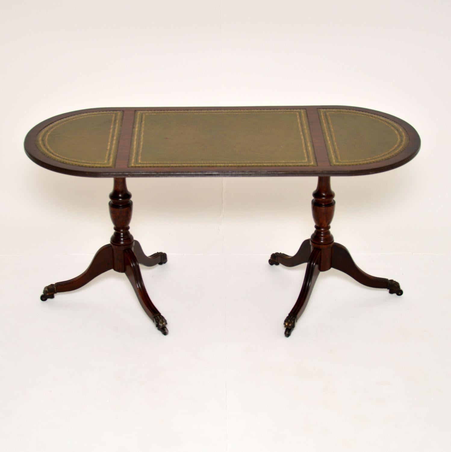 A beautiful and elegant antique Regency style coffee table in wood. This was made in England, it dates from around the 1950’s.

It has a lovely design, with an oval top and two splayed tripod bases. There is a three section gold tooled leather