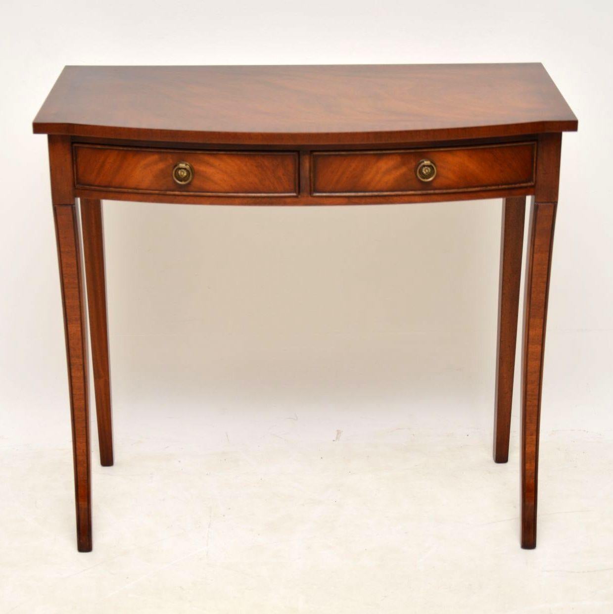 Antique Regency style mahogany side table in good condition and dating from the 1950s period. It has a cross banded flame mahogany top, two drawers with brass handles and sits on sabre legs. This table could be used as a side table or even a writing