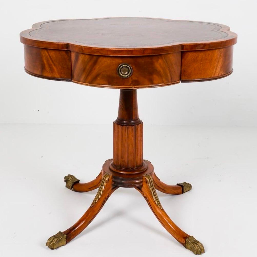 Elegant Regency style drum table featuring a scalloped edge top and tooled leather.  Add a touch of sophistication to any room.  Includes functional drawer and is supported on a fluted pedestal base and adorned with striking brass paw feet with