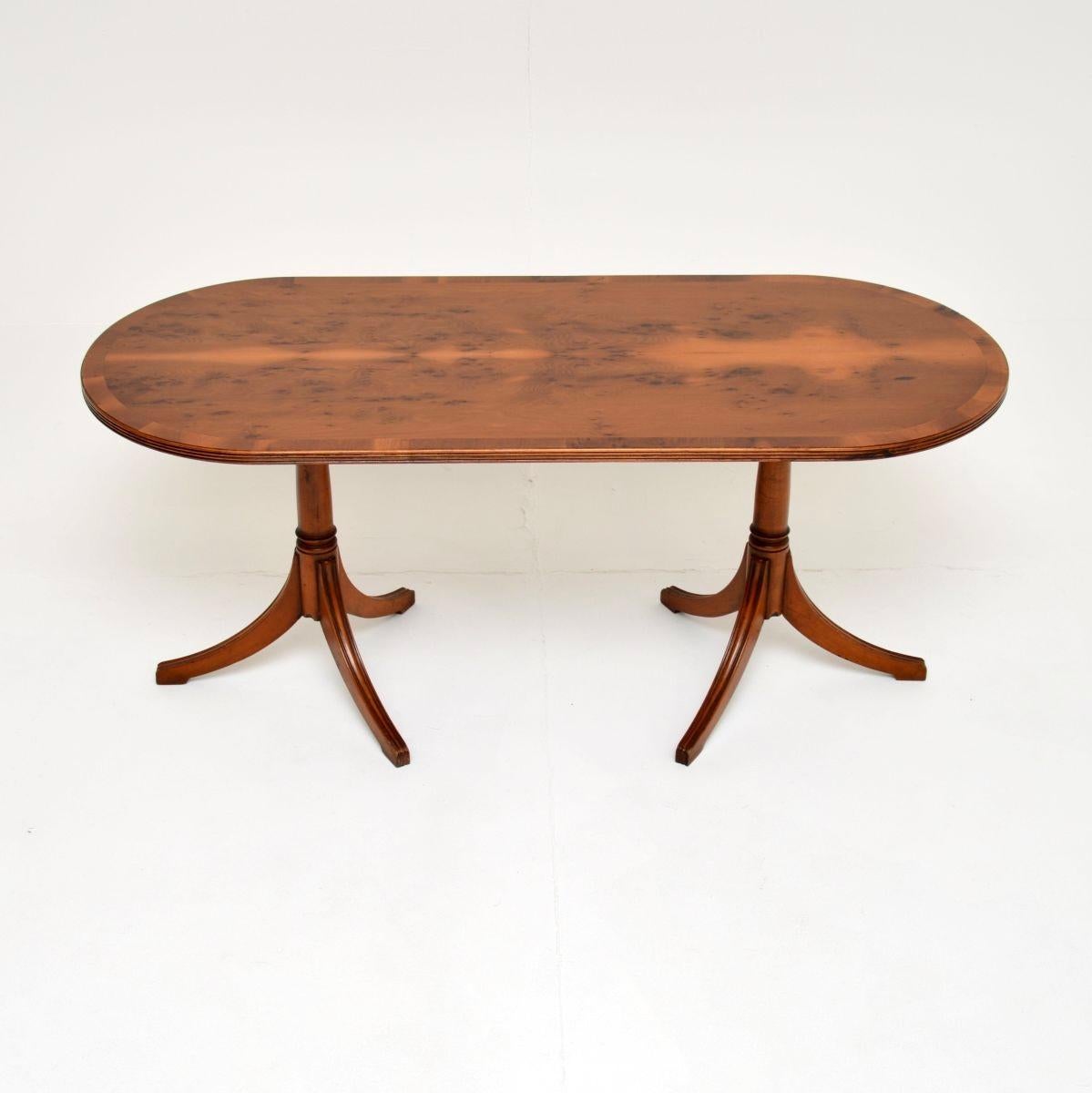 Cette table basse en bois d'if de style Regency a été fabriquée en Angleterre et date des années 1950.

Il est d'une superbe qualité, le plateau ovale a des bords à bandes croisées et de beaux motifs de grain. Il repose sur deux socles tripodes