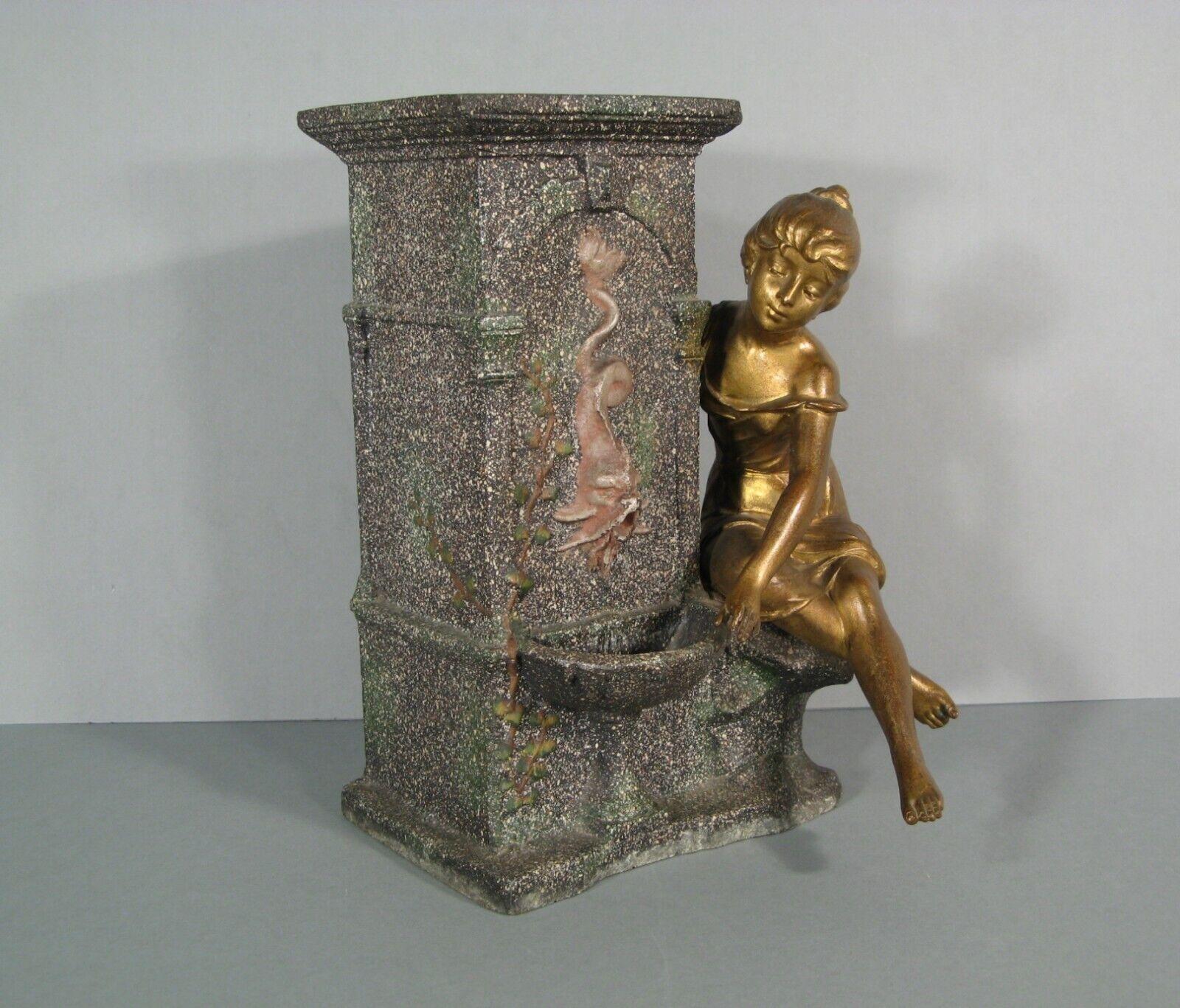 Elevate your home decor with this highly decorative antique vase, crafted from patinated régule and pewter. This exquisite piece, inspired by the style of Moreau, features a young woman seated at the edge of a fountain adorned with a dolphin, making
