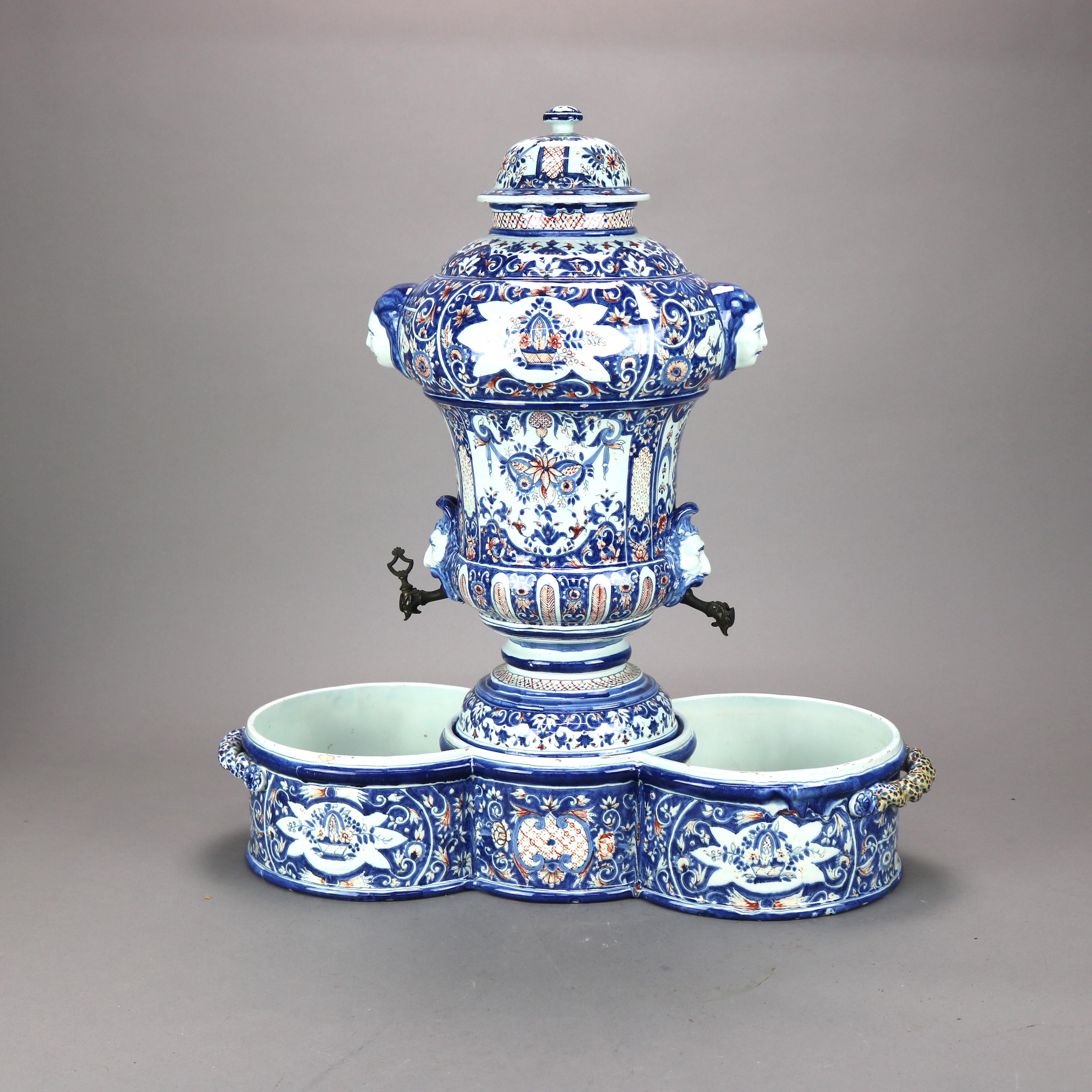 An important Rouen, France Faience cistern and basin decorated by Jean Claude Borne offers faience soft paste porcelain pottery construction with vessel in urn form and having polychromed foliate, scroll and floral decoration, flanking figural masks