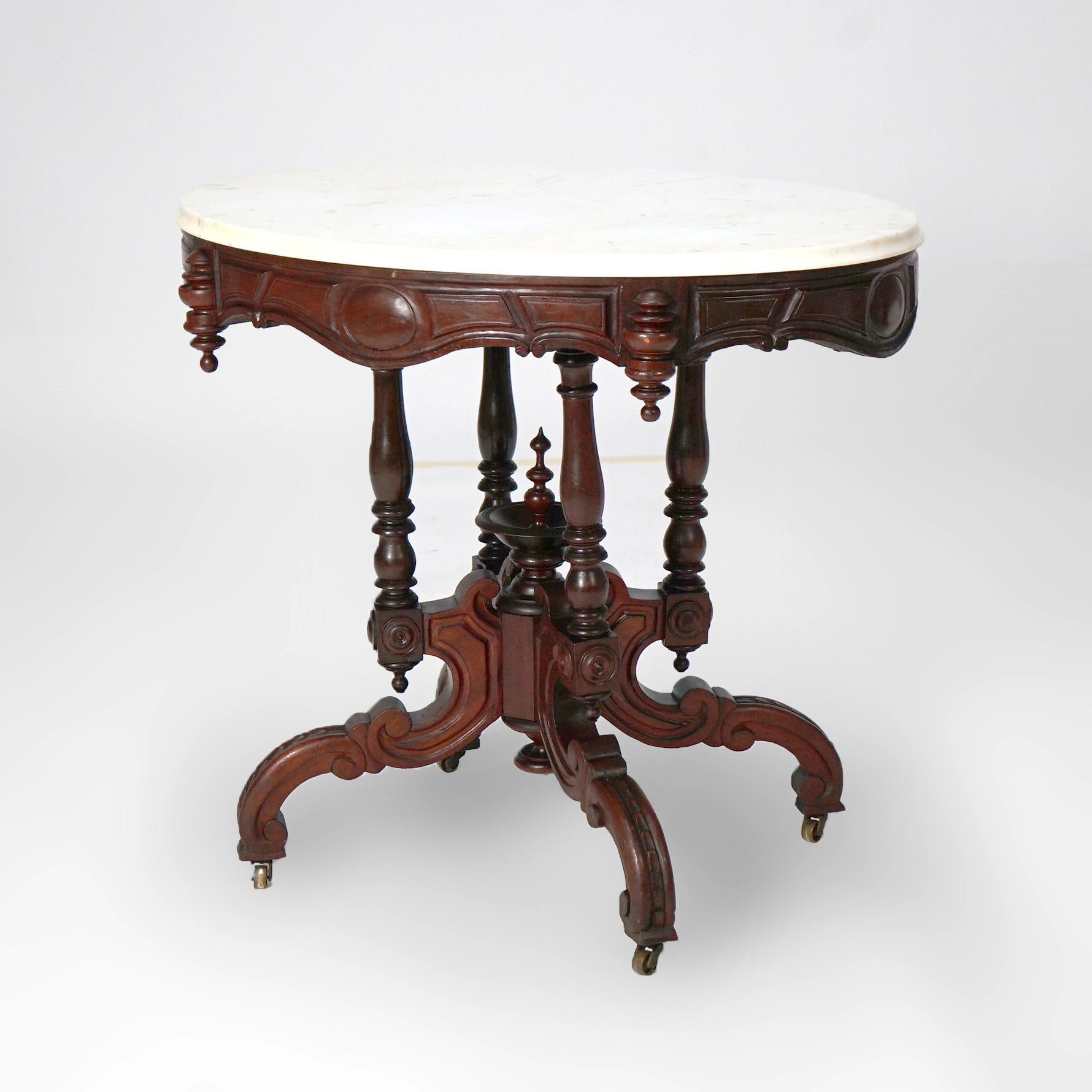 An antique Renaissance Revival Brooks parlor table offers beveled oval marble top over carved walnut base with shaped skirt having medallions and drop finials,  turned balustrade supports with central urn form finial, and raised on scroll form legs,