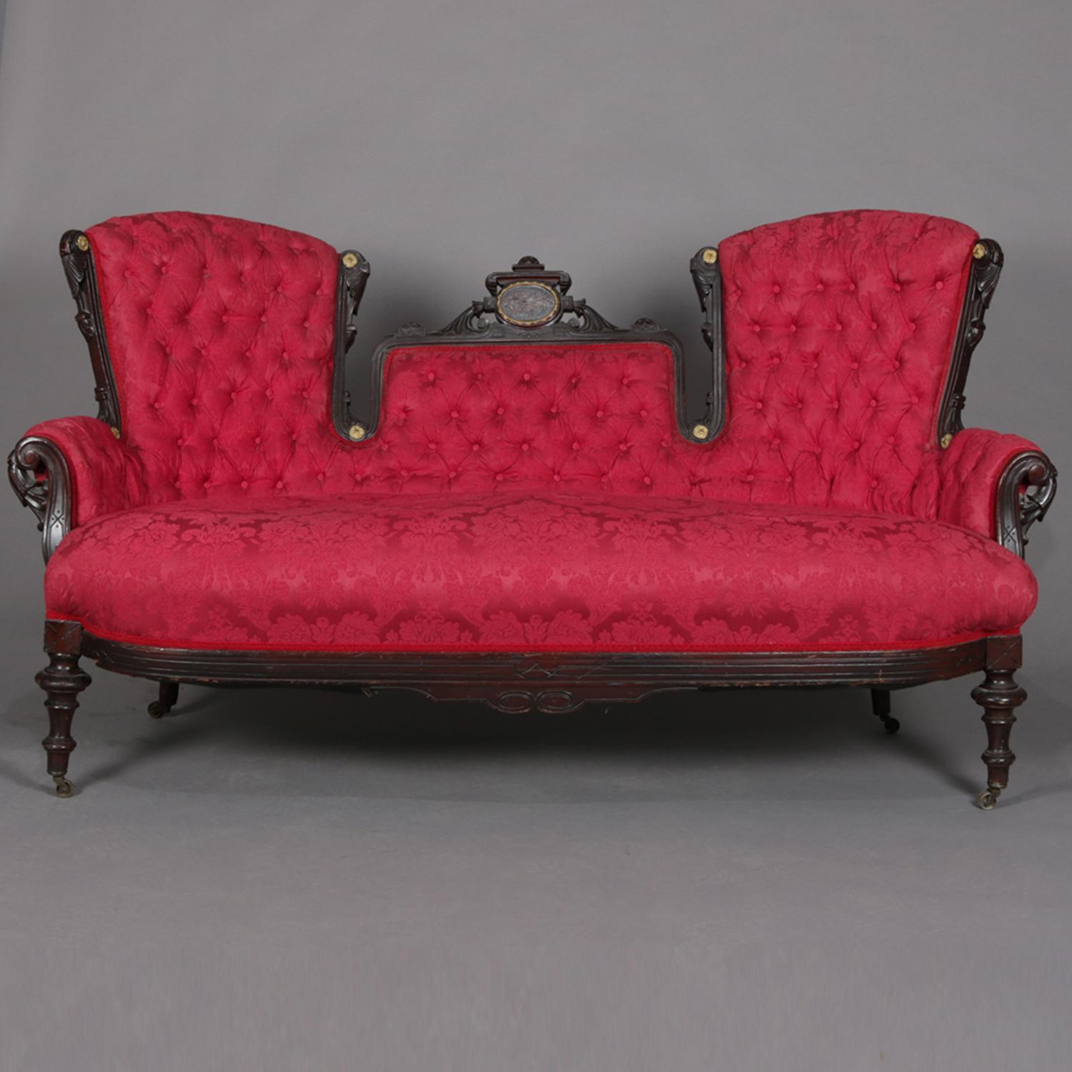 Antique Renaissance Revival Jelliffe School triptych sofa features carved frame with segmented back including crest with foliate inlaid medallion with gilt bordering, gilt rosettes throughout, and foliate scroll form arms, button back upholstered