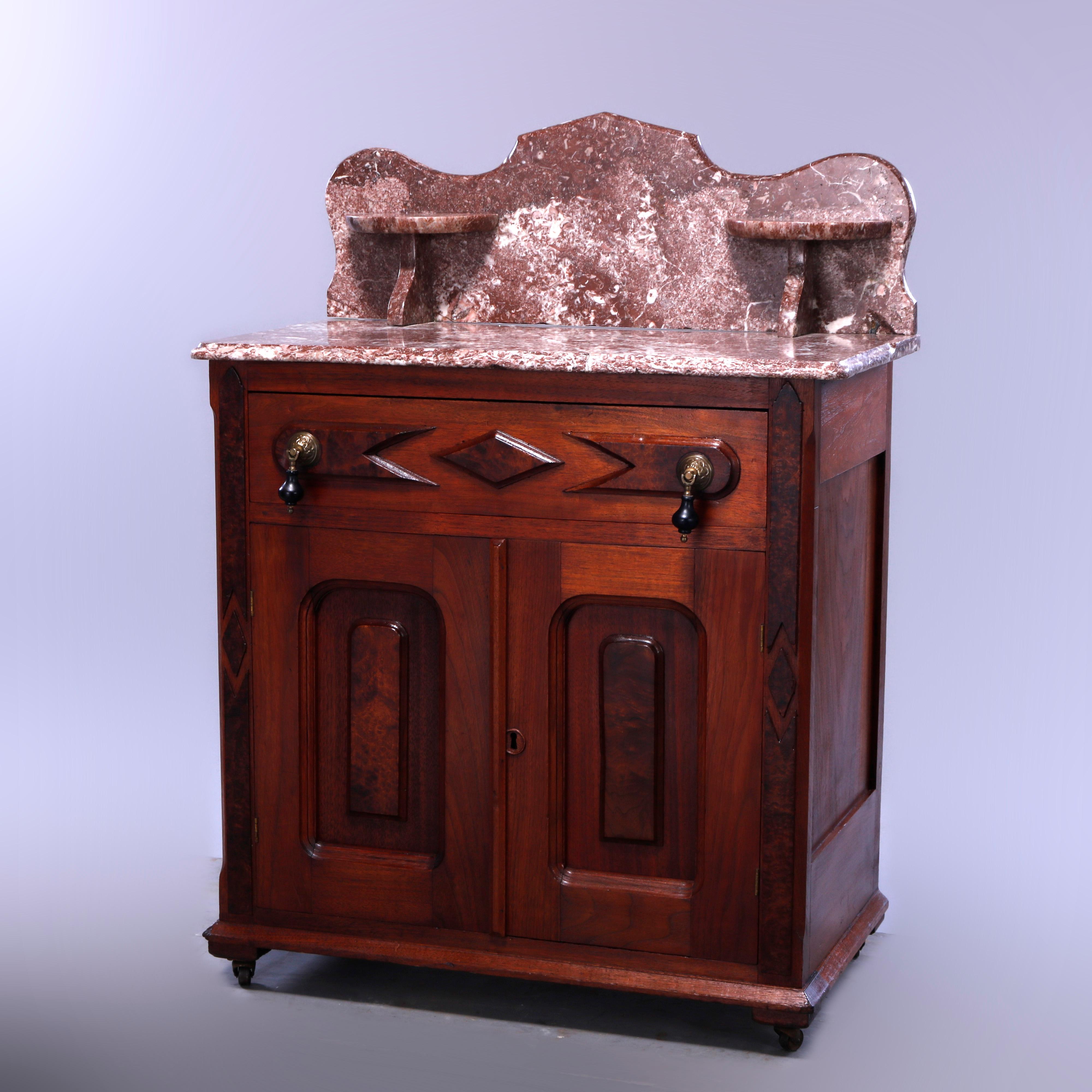 An antique Renaissance Revival wash stand commode offers walnut construction with rouge marble top having shaped backsplash with flanking candle stands surmounting case with frieze drawer over double door lower cabinet, raised panels throughout,