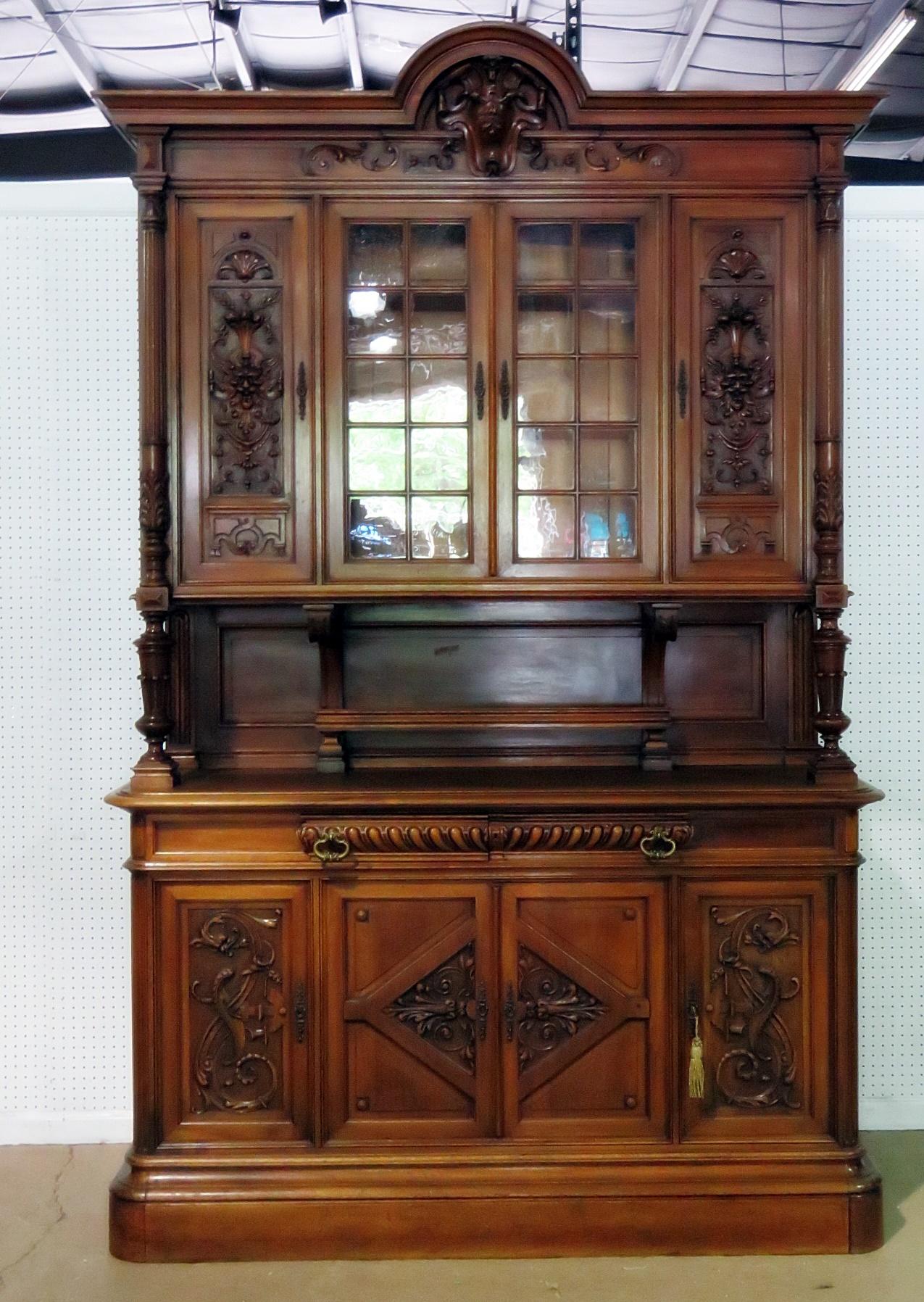 Antique Renaissance style two-piece china cabinet. The top has four doors containing two shelves. The bottom has two drawers over four doors containing one shelf.