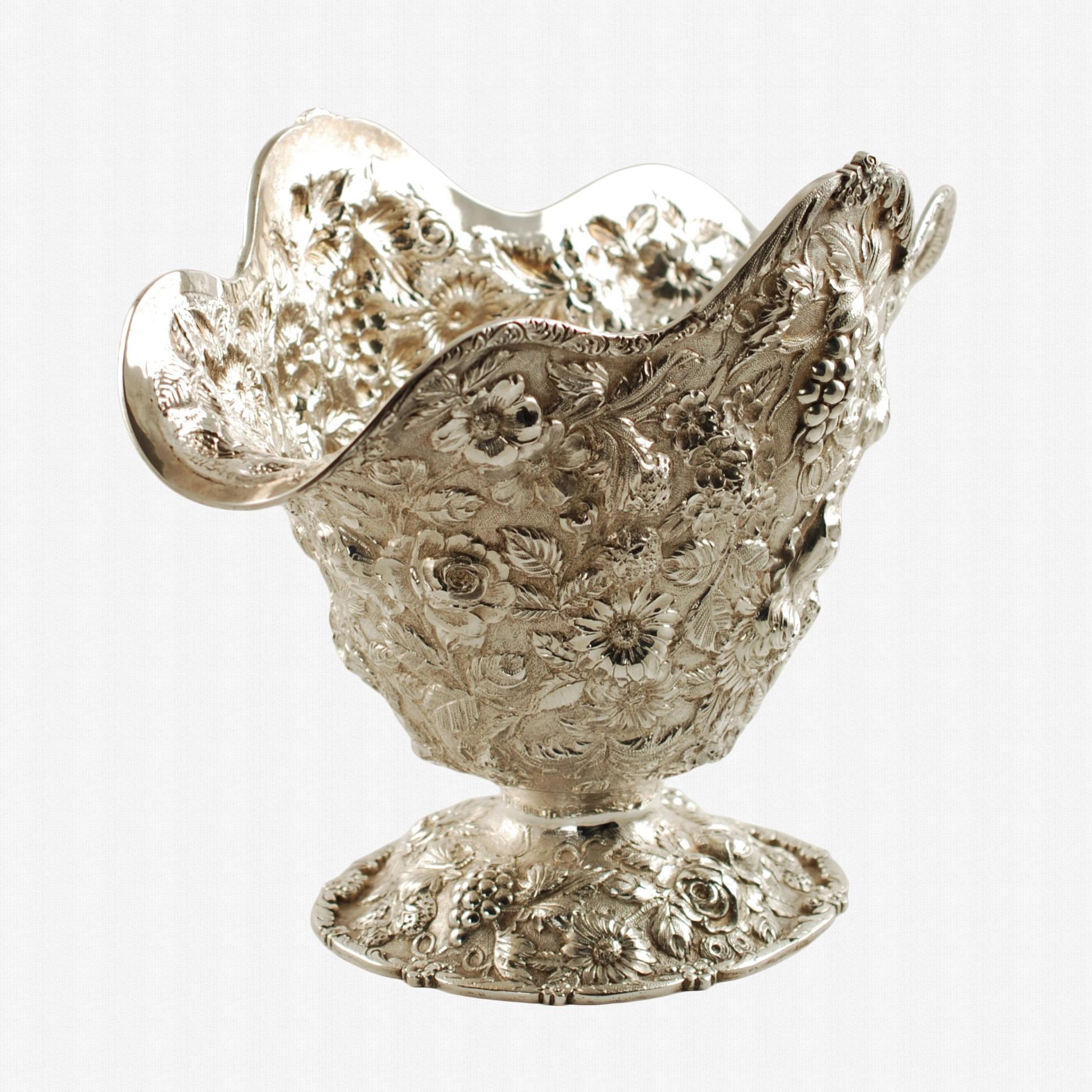 Diese exquisite Schale mit Fuß aus Sterlingsilber von Loring Andrews aus dem frühen 20. Jahrhundert weist ein handziseliertes Repoussé-Dekor auf, das aus zahlreichen Blumen, Erdbeeren und Trauben sowie Blättern und geschwungenen Ranken besteht, die