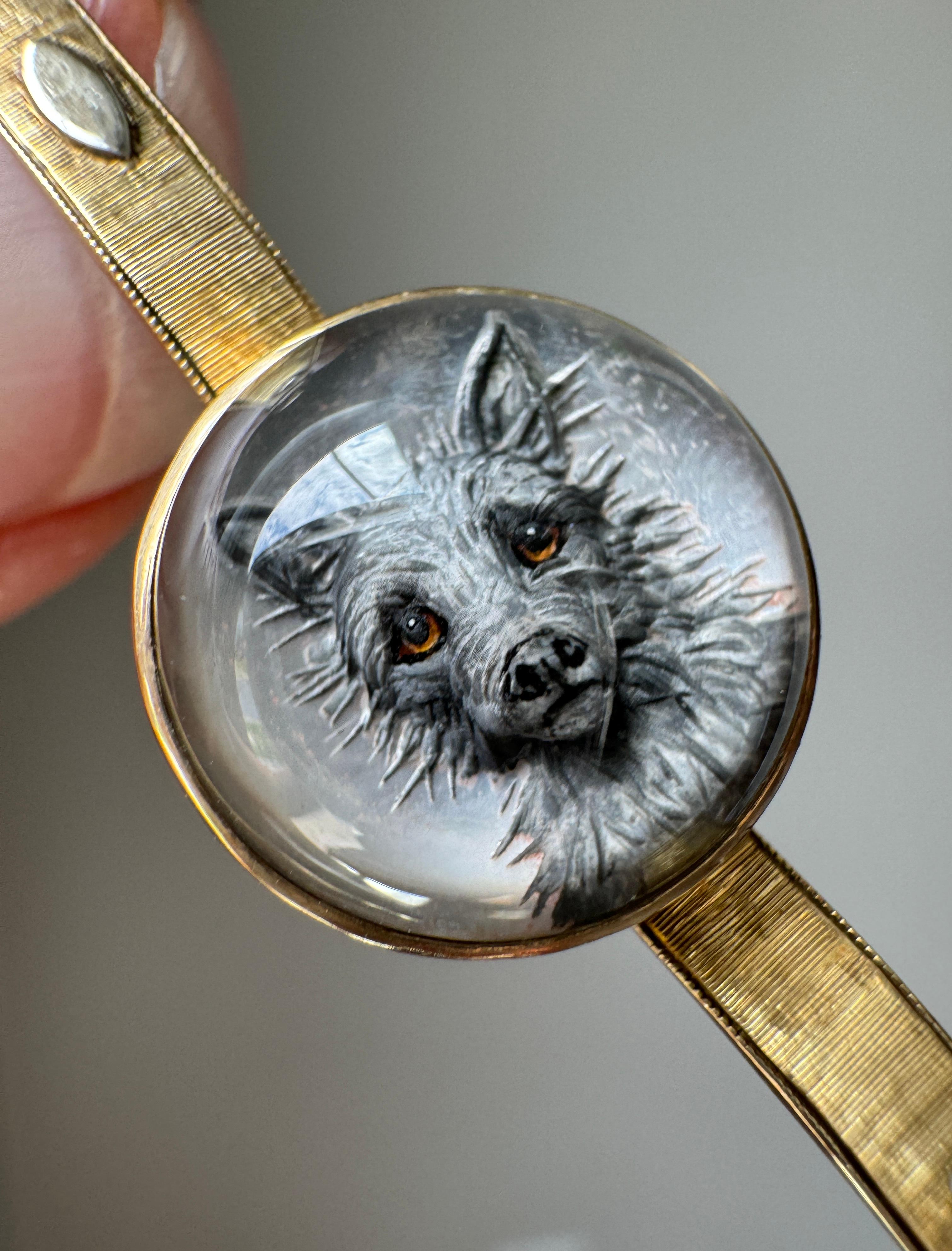 Este terrier tridimensional deliciosamente desaliñado ha sido tallado en calcografía en un cabujón de cristal de roca y detallado a mano con finos pinceles. El cabujón está respaldado por un disco de nácar brillante y centrado en un collar de oro