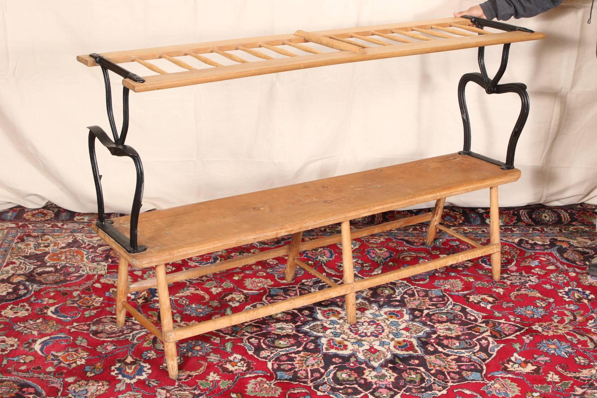 Antique reversible bench, pine, spindle back and black painted iron arms, long stretchers front and back and cross stretchers front to back, raised on splayed cylindrical legs. 

Condition: Expected surface wear and signs of use including some