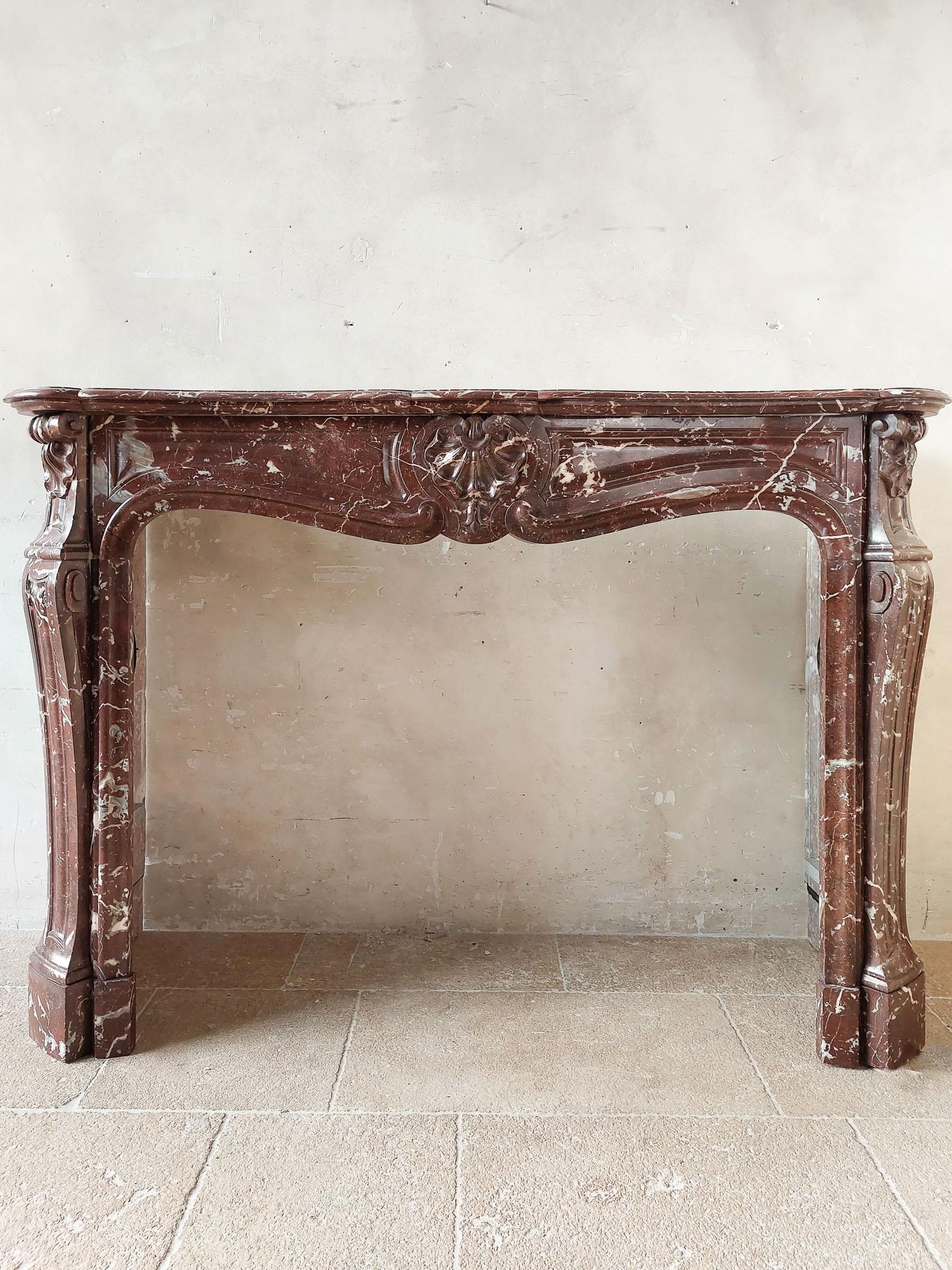 Antique, rich, hand-carved Trois Coquilles mantelpiece in red marble, with gray and white accents (campan rouge marble).

dimensions: h 116 x w 166 x d 20.5 to 38.5 cm
internal dimensions: h 90 cm x w 121 cm