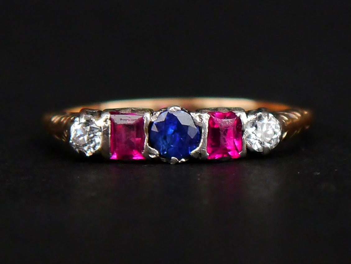 Ring in solid 18K Yellow Gold decorated with a row of natural Rubies, Diamonds and a natural Blue Sapphire.

Old European diamond cut Diamonds Ø 3.5 mm / 0.21 ct each / color F,G /VS

Baguette cut Rubies ca 3.5 mm x 2.75 mm /ca 0.15 ct