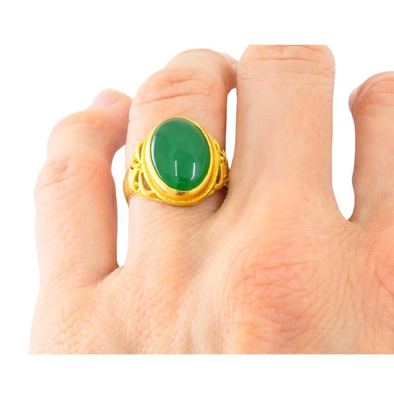 A refined Antique ring, featuring jade, made of 18k gold. 
The cabochon jade set in a delicate open-work mounting, adorned with intricate filigree style cutouts on either side. A subtle migraine detail frames the bezel, adding a sense of lightness