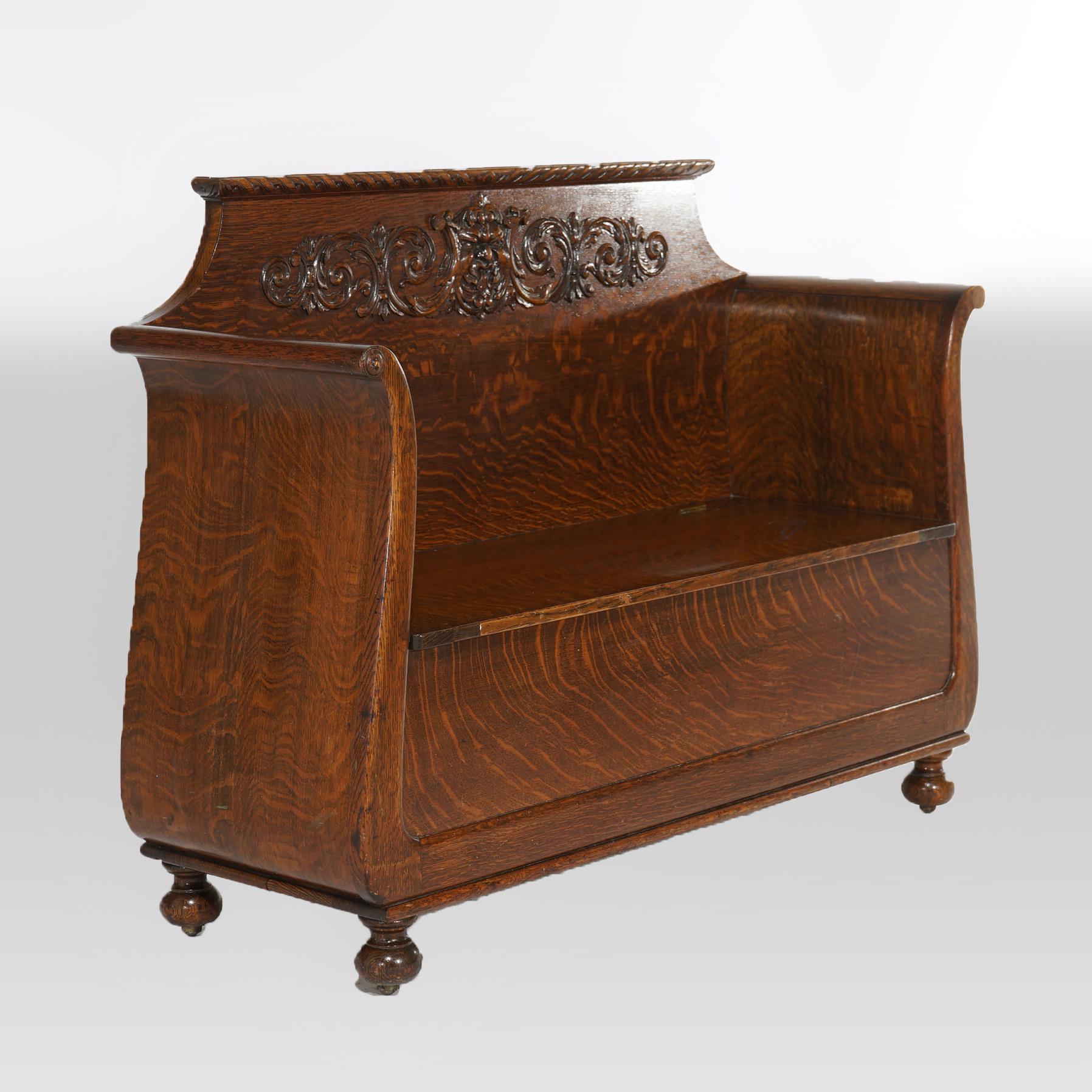 An antique hall bench in the manner of RJ Horner offers quarter sawn oak construction with back having carved wind god with flanking foliate elements over lift-top seat with flanking scroll form arms, raised on ball feet, c1900

Measures- 40.75''H x