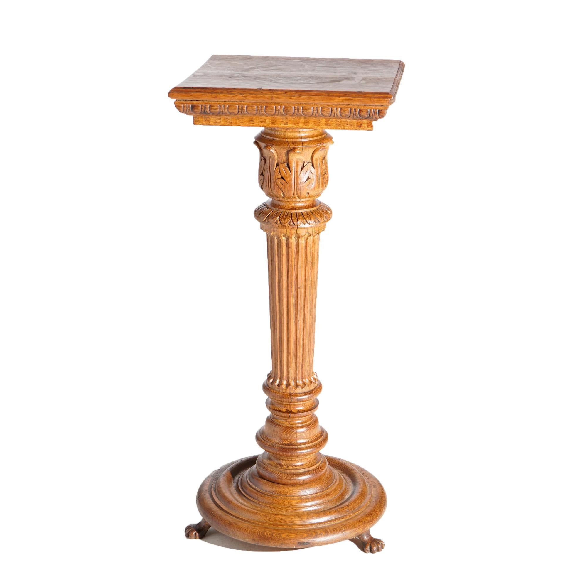 An antique sculpture pedestal in the manner of RJ Horner offers quarter sawn oak construction with square display over stylized and tapered Greek Corinthian column with carved acanthus capital raised on platform with carved paw feet,