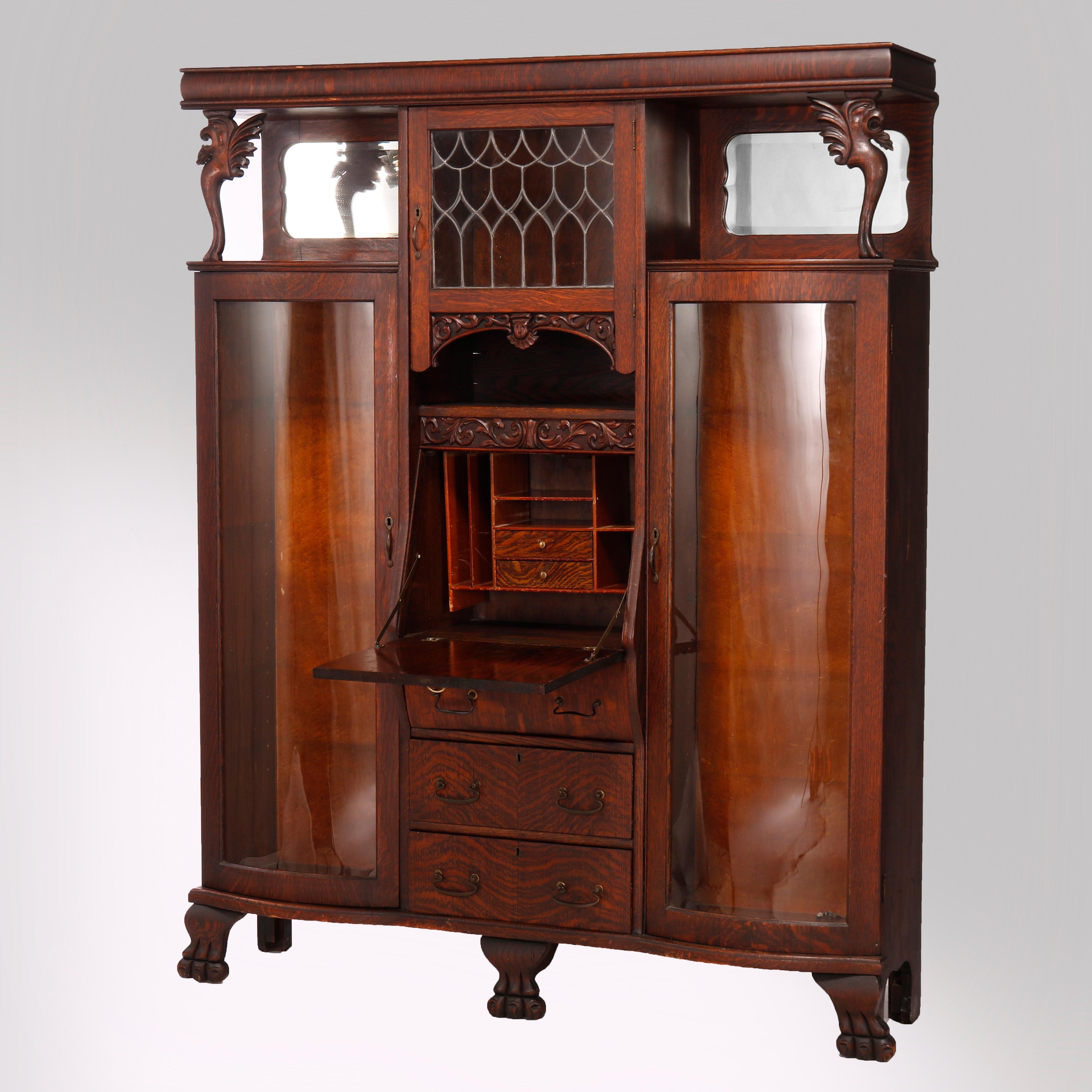 An antique double secretary in the manner of RJ Horner offers quarter sawn oak construction with upper central cabinet having leaded glass door and flanking open shelves with shaped and beveled mirrors, over central secretary with drop down desk