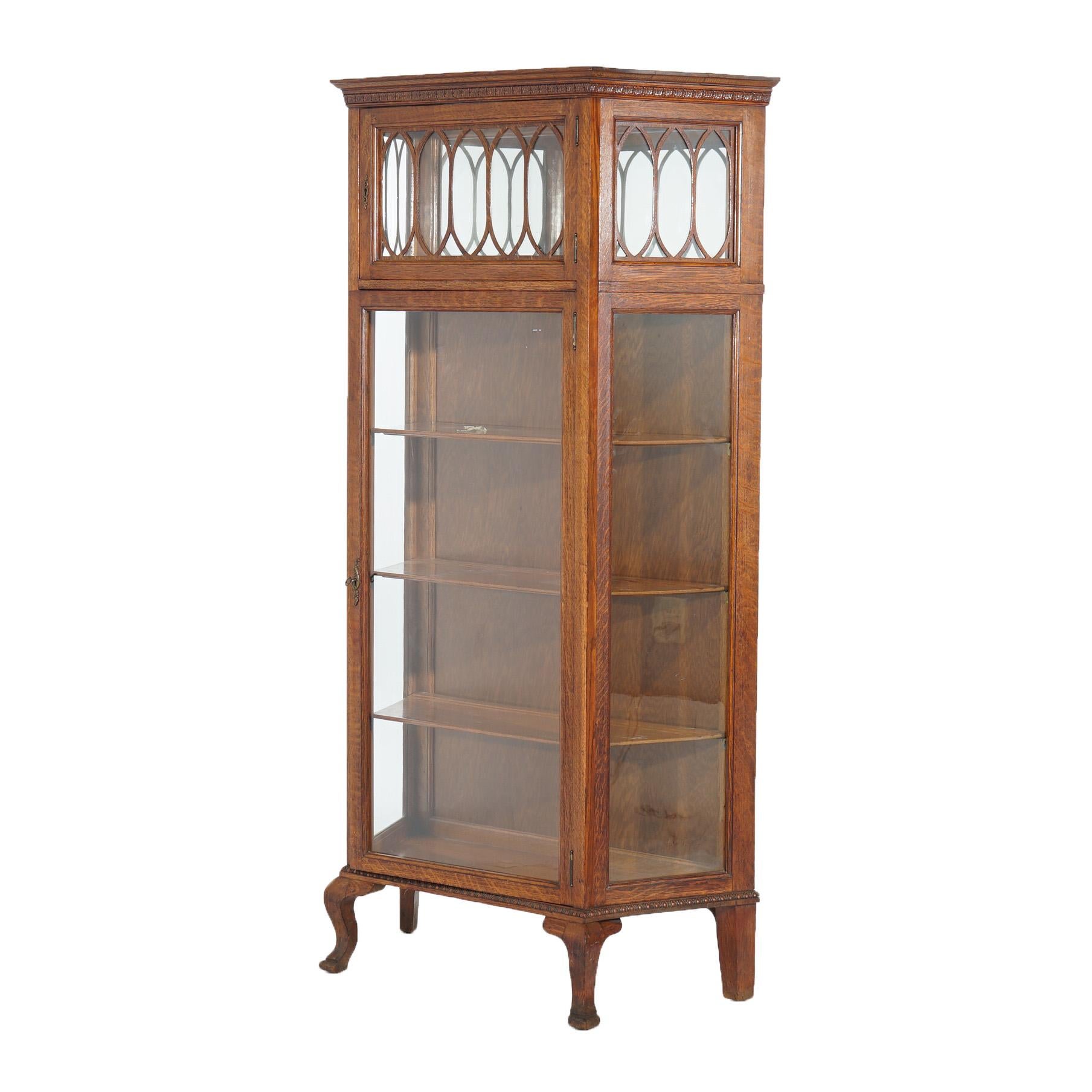 An antique double curio in the manner of RJ Horner School offers oak construction with upper display having leaded glass door opening to mirrored compartment and single door over lower cabinet having single door opening to shelved interior, raised