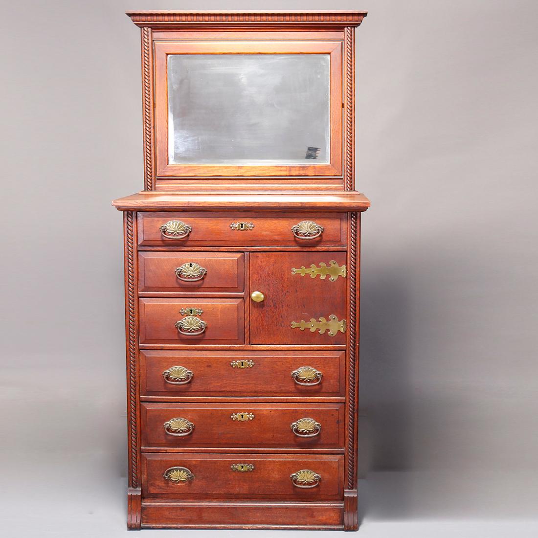 An antique chest of drawers in the manner of RJ Horner offers oak paneled construction with mirror surmounting drawer tower with hat box and carved rope twist trimming, c1900

Measures: 77