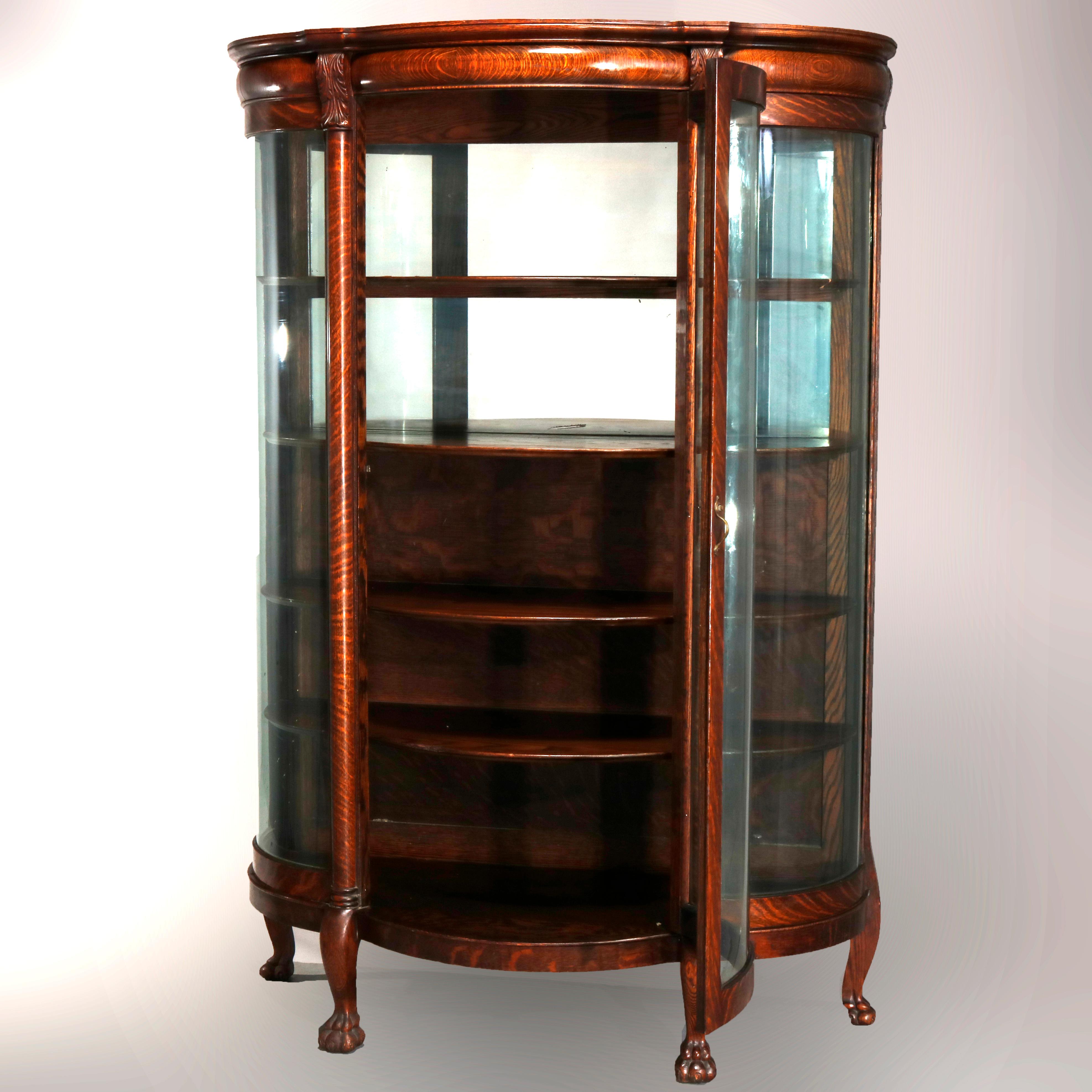 An antique China cabinet in the manner of R.J. Horner offers quarter sawn oak construction in serpentine form having bowed glass door and sides, mirrored and shelved interior, raised on cabriole legs terminating in paw feet, carved acanthus foliate