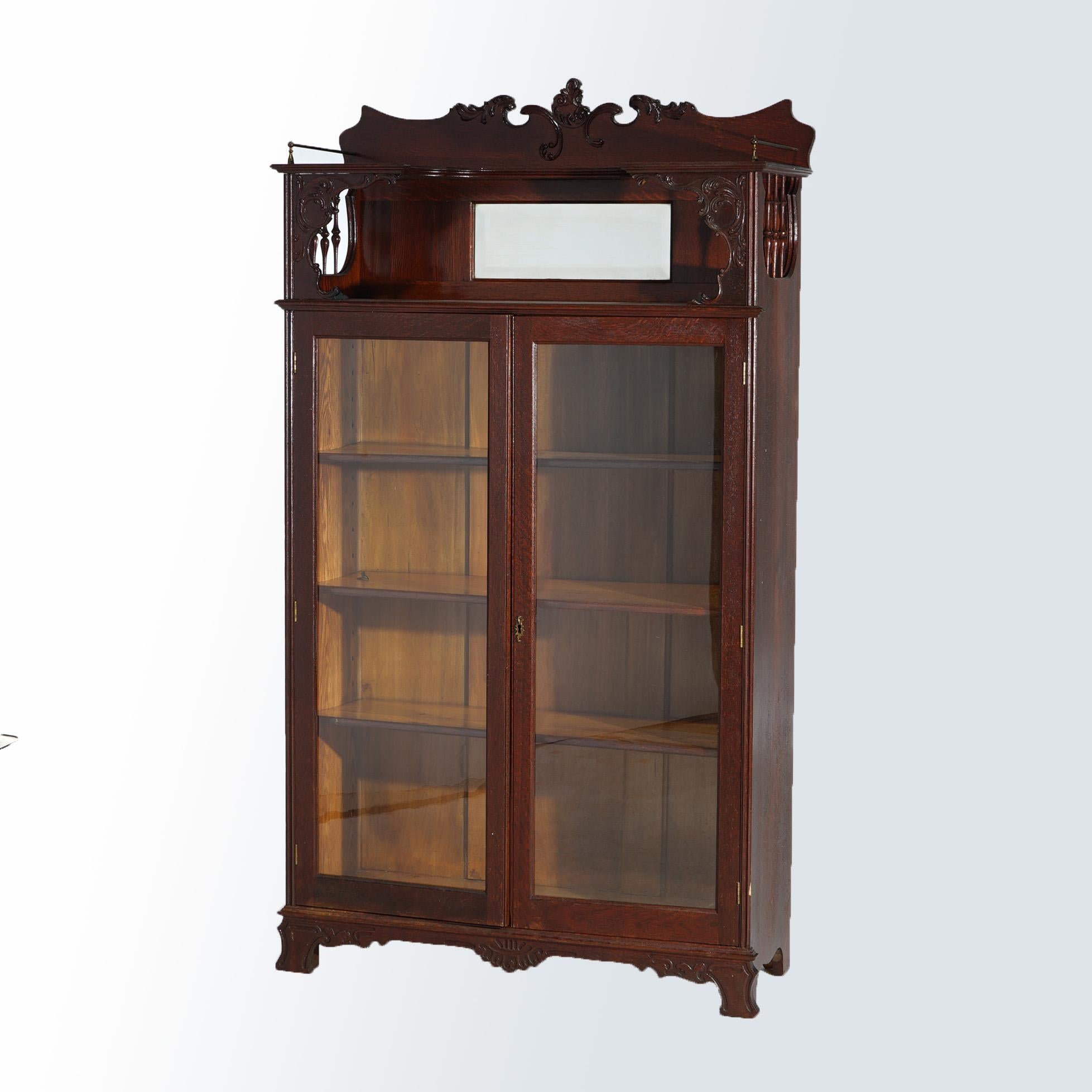 ***Ask About Lower In-House Shipping Rates - Reliable Service & Fully Insured***
An antique bookcase in the manner of RJ Horner offers oak construction with mirrored crest having scrolled frame, spindle supports and surmounting double glass doors