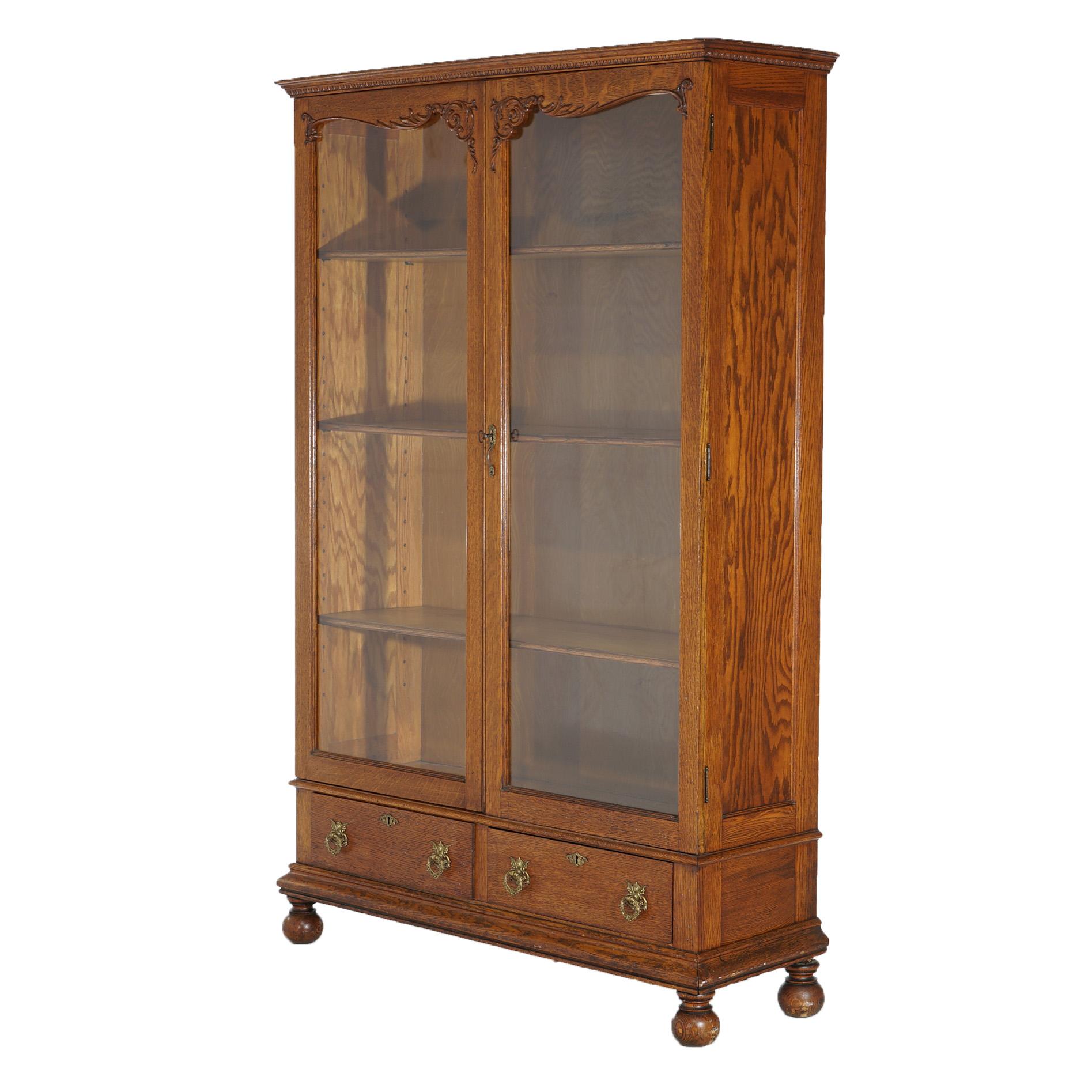 An antique bookcase by Skandia and in the manner of RJ Horner offers quarter sawn oak construction with double glass doors having carved foliate elements and opening to a shelved interior over two lower drawers, and raised on bun feet, en verso