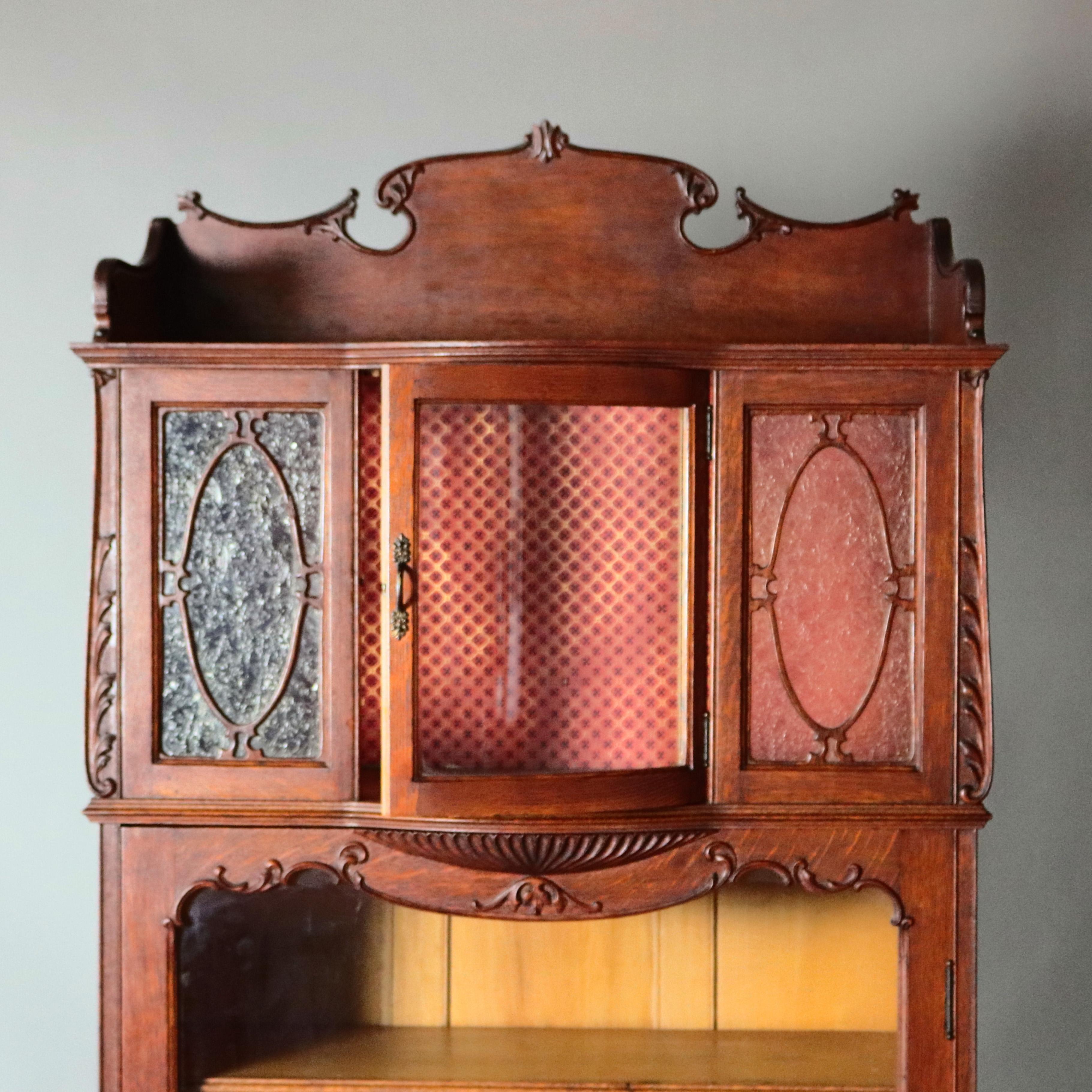 An antique R. J. Horner School Victorian cabinet offers case with shaped backsplash surmounting upper curio having door with curved glass flanked by carved oak filigree panels and foliate bordering and lower bookcase with single glass door, circa