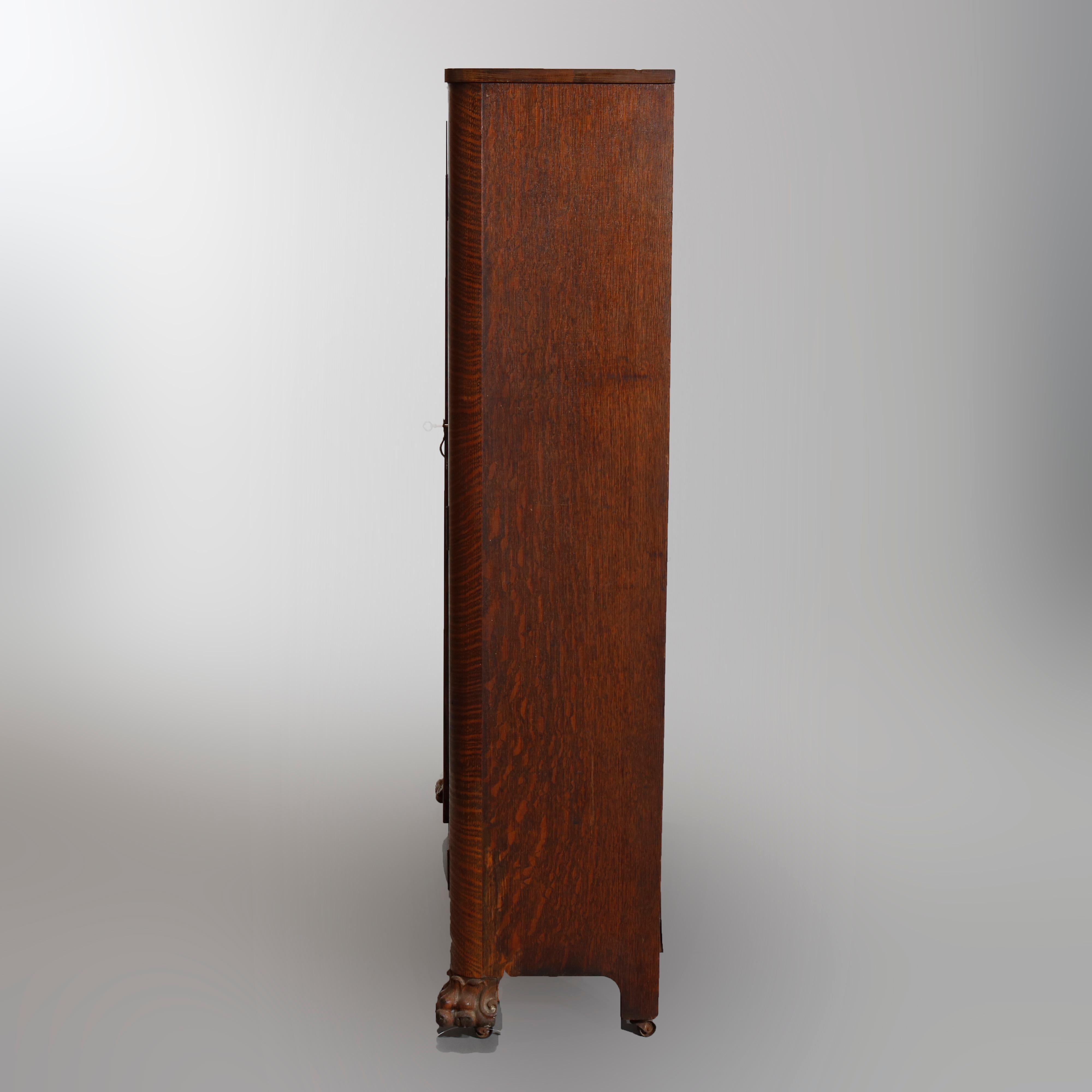 An antique bookcase in the manner of RJ Horner offers quarter sawn oak construction with double glass doors opening to shelved interiors, raised on carved claw feet, circa 1910

Measures: 56.5