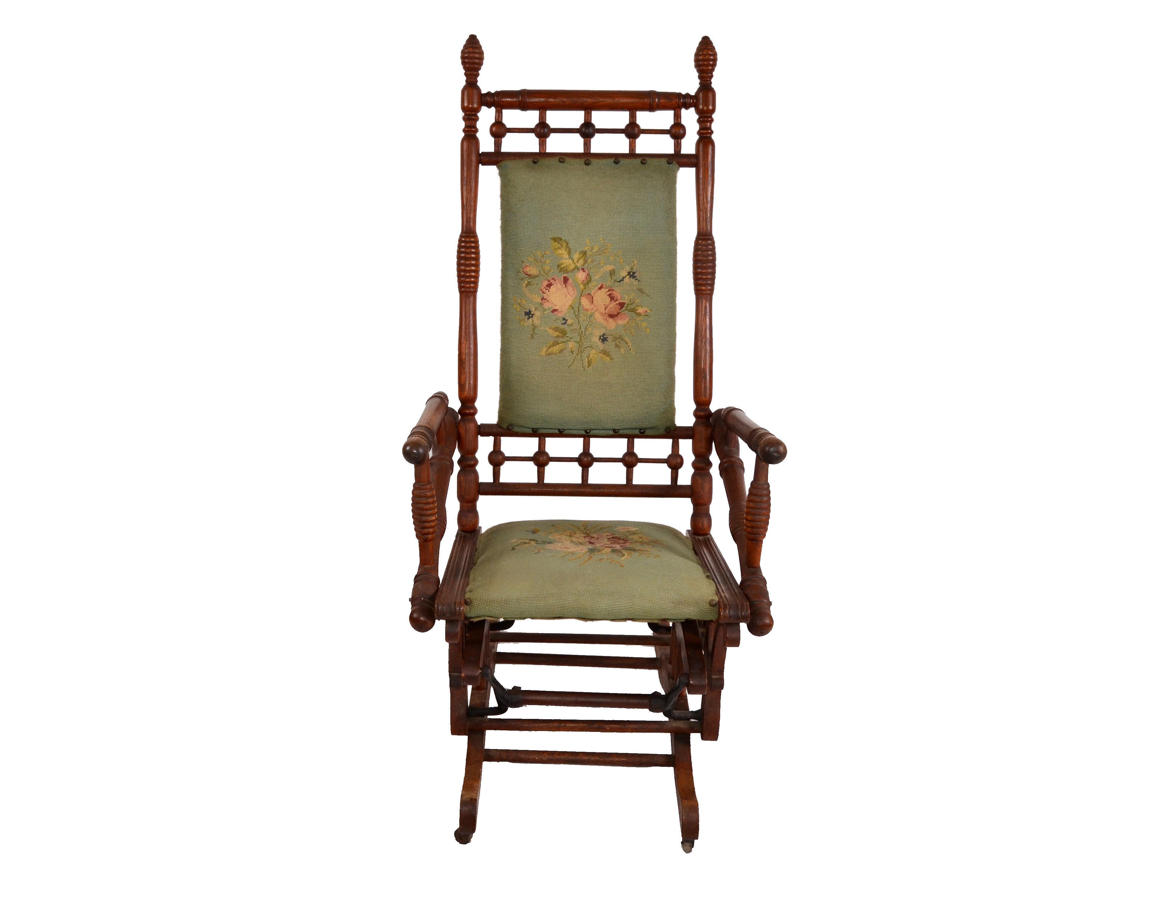 Rocking chair from the late 19th century, hand carved with turned wood details on 2 casters.
Sturdy and comfortable crafted frame with decorative rocking base.
Nailhead trim adorn the handmade needlepoint upholstered seat and chair front.
Measures:
