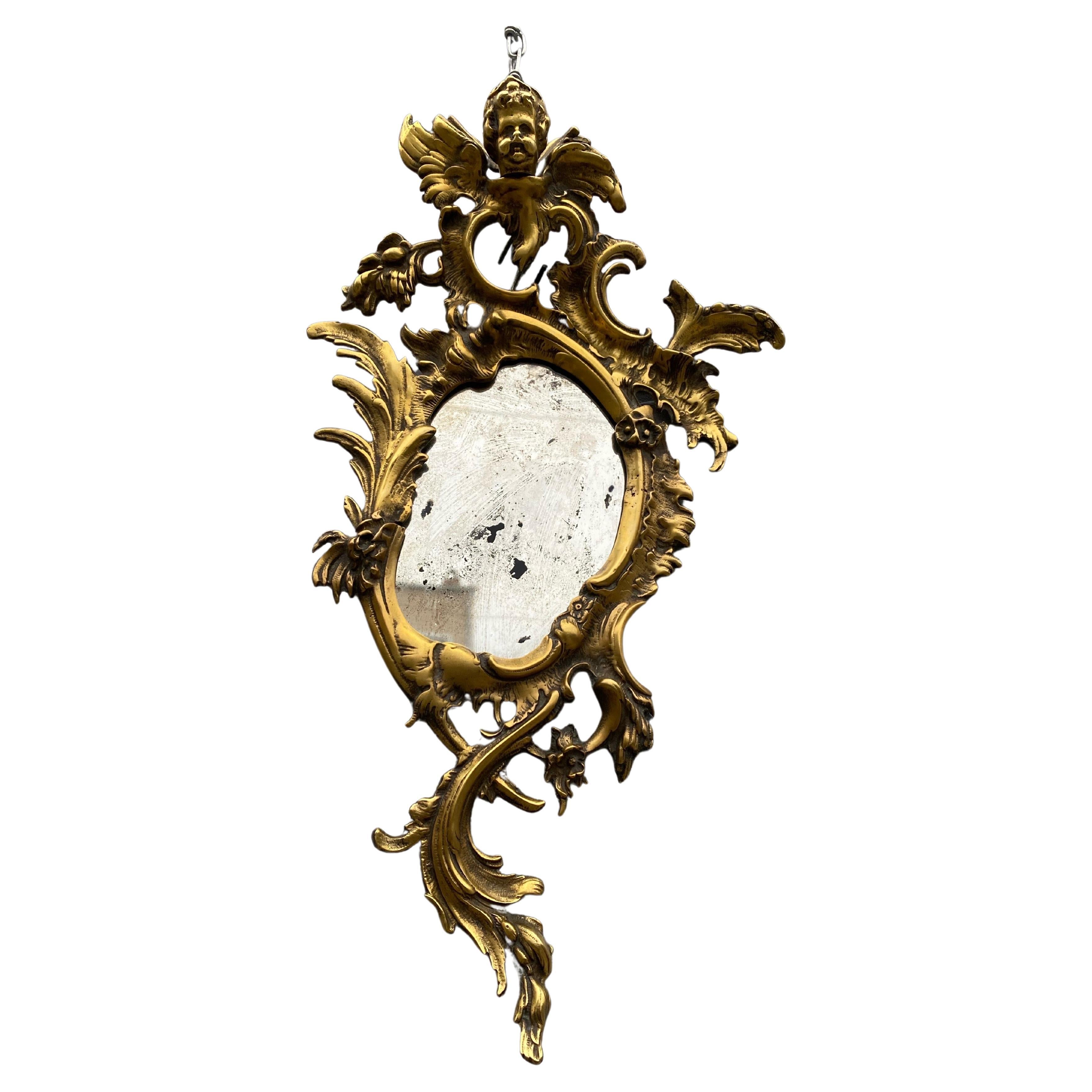 Antique Rococo figural bronze wall mirror.

This is a small bronze wall mirror featuring intertwined scrolls of acanthus leaves. It is embellished by a winged cherub bust as a finial.

circa 1880

Dimensions 

W 12”
H 23”

Mirror 

W