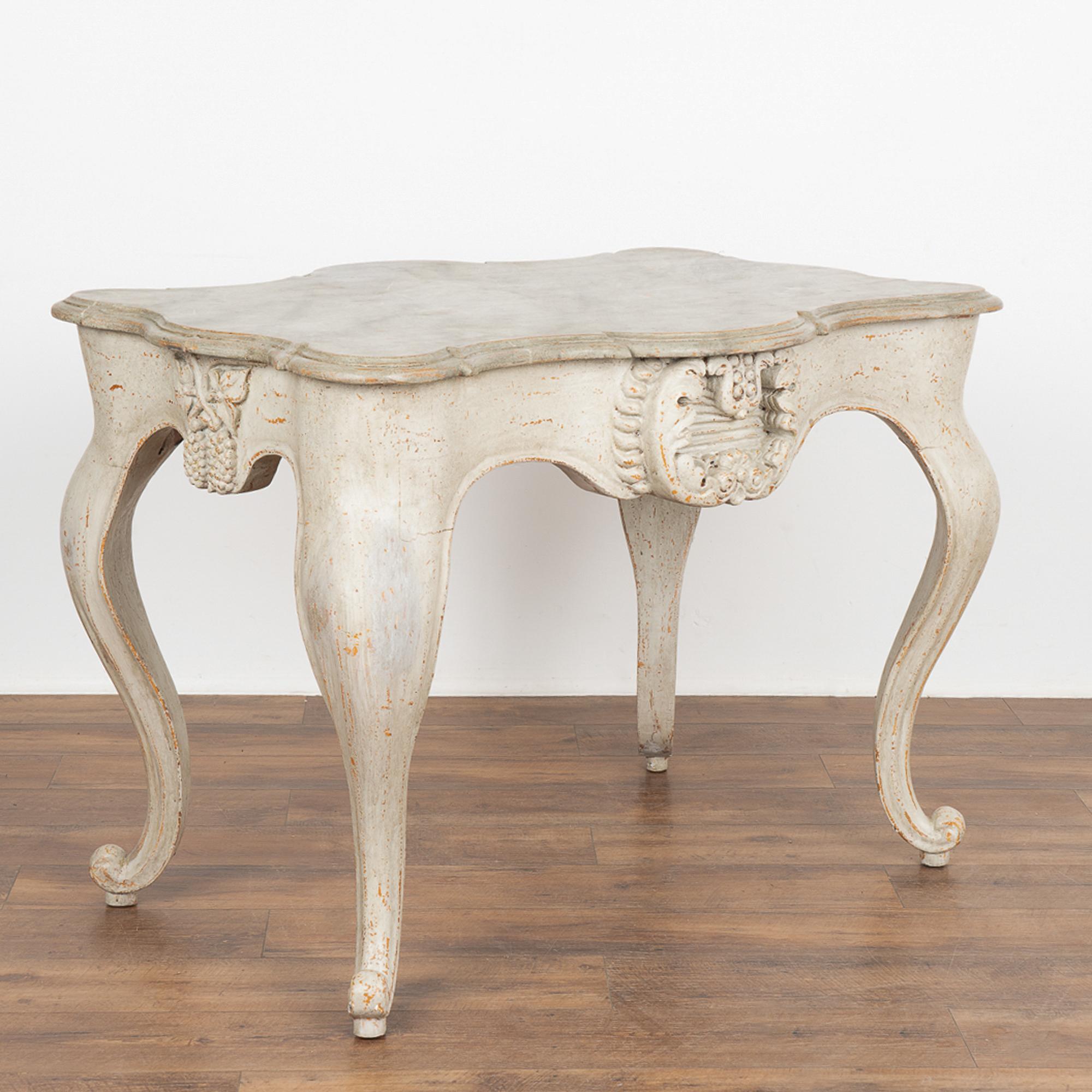 This rococo pine table has dramatic cabriolet legs and heavily carved flourishes that embellish the scalloped skirt. 
The gray painted finish is lightly distressed adding to the aged grace of this striking accent table. The top is painted in