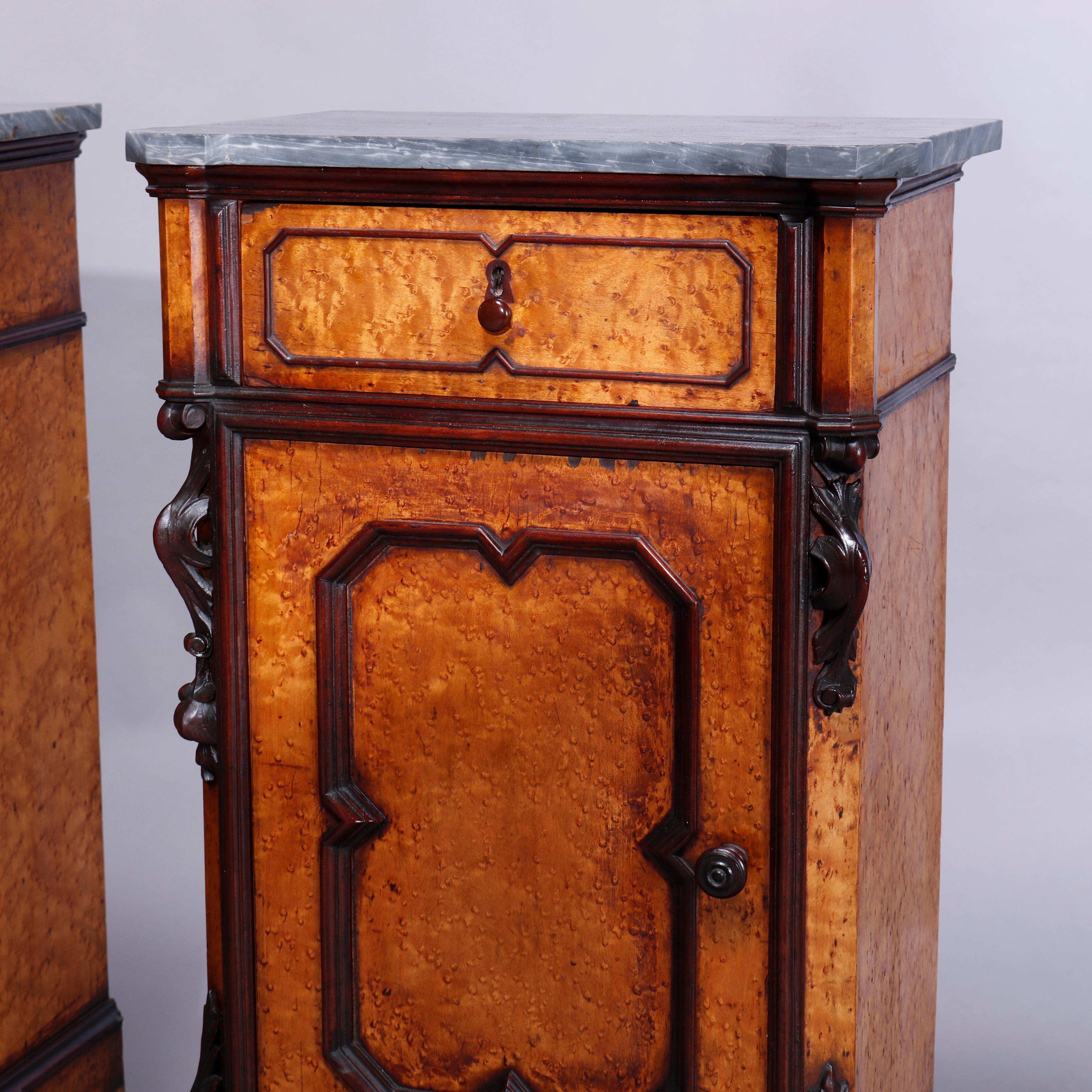 An antique pair of French Rococo Revival side stands offer shaped marble tops over birdseye maple and walnut cases having paneled single upper drawers and lower single door cabinets opening to shelved interiors, raised on Mersailles bun feet, carved
