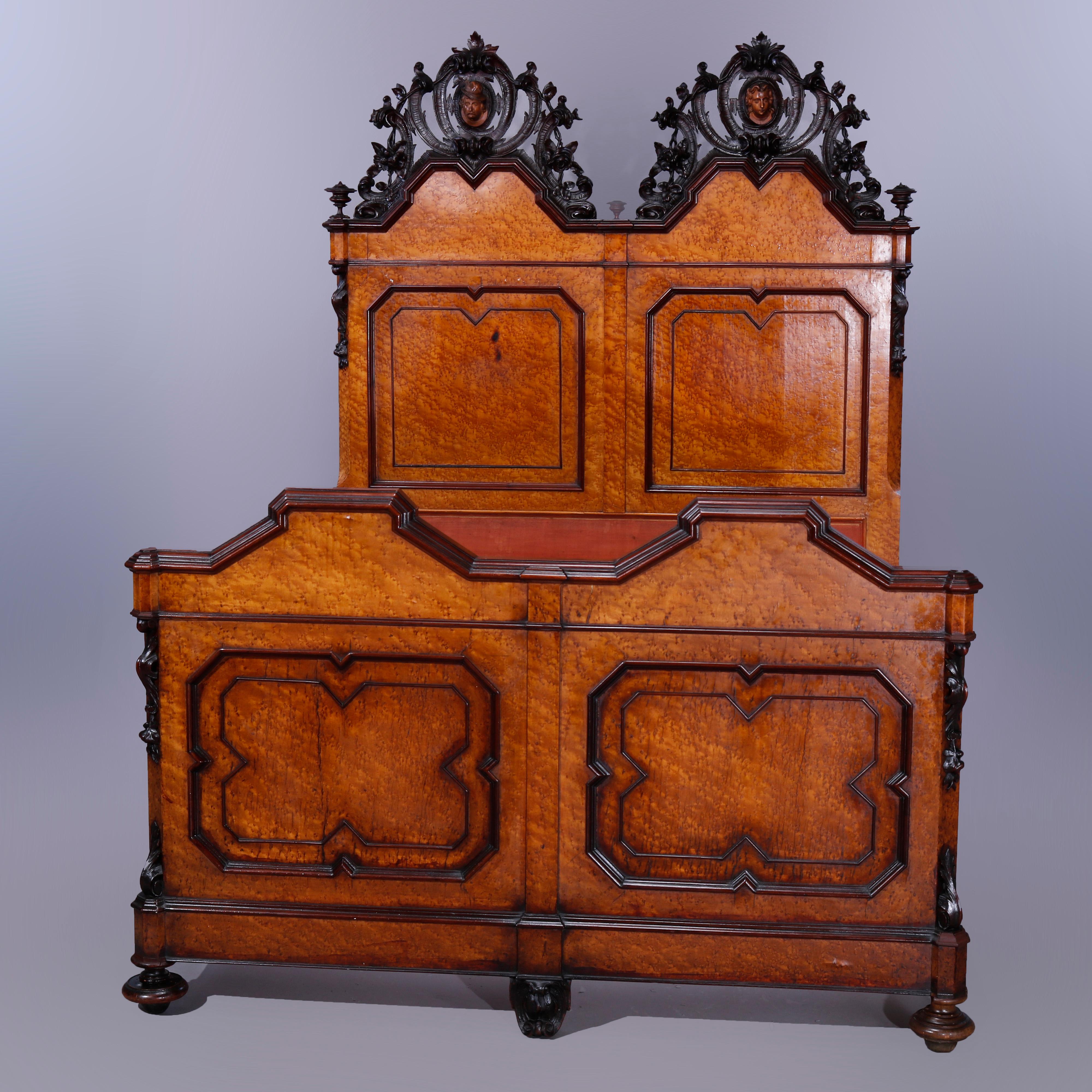An antique Rococo Revival figural double or full size bed offers birdseye maple construction with heavily carved and pierced foliate walnut crest with central masks and flanking urn form finials over paneled headboard with walnut trimming, raised on