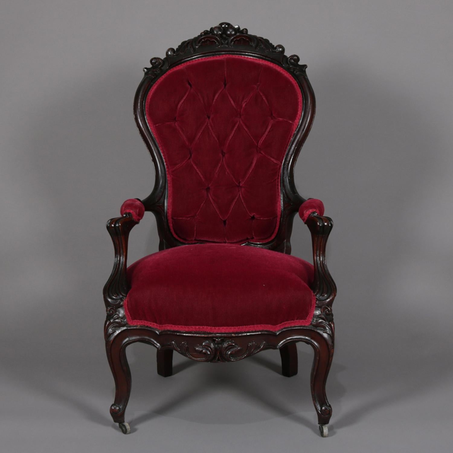 An antique Victorian Rococo Revival armchair features carved walnut frame with balloon back having pierced floral crest and button back velvet upholstery, raised on cabriole legs, circa 1890.

Measures: 44