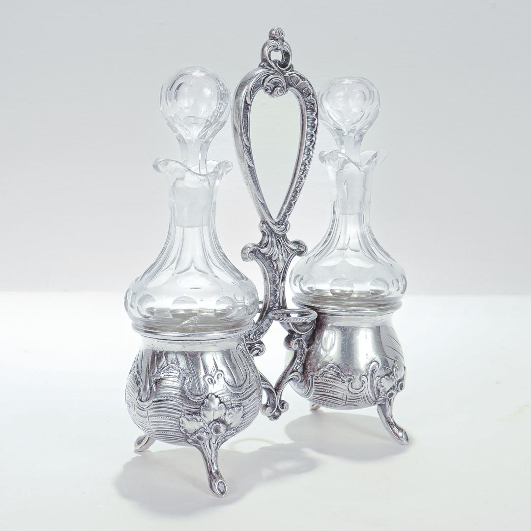Un raffinato set di ampolle antiche.

In argento fine 800 a grana sottile.

Con bottiglie e tappi in vetro tagliato.

Il supporto è composto da due ciotole o coppe vasiformi decorate a rocaille, sostenute da piedi a foglia e ramoscello e unite da
