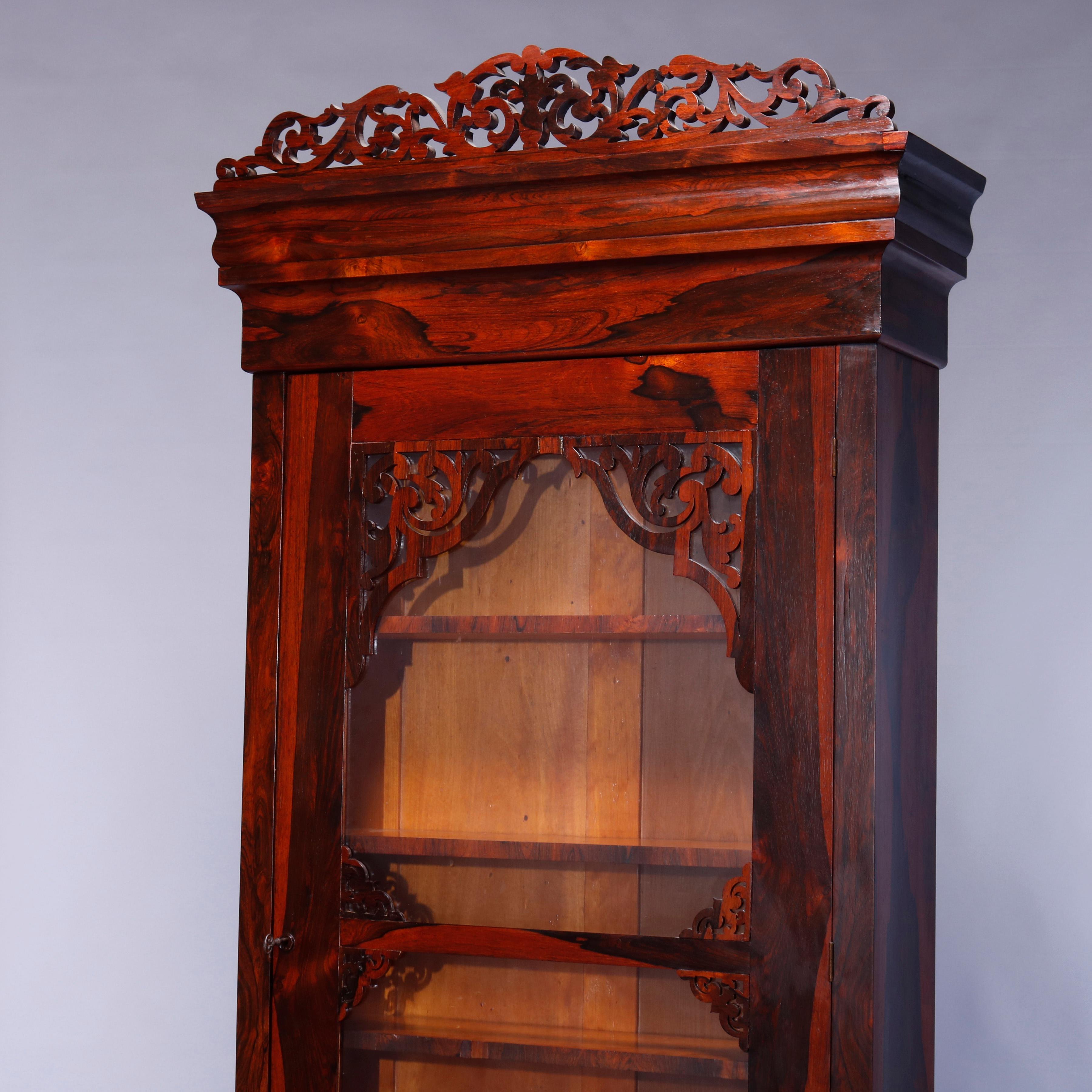 An antique Rococo Revival bookcase offers rosewood construction with pierced foliate filigree crest surmounting case with single glass door also with foliate filigree and opening to shelved interior, seated on single drawer base, c1880.

Measures: