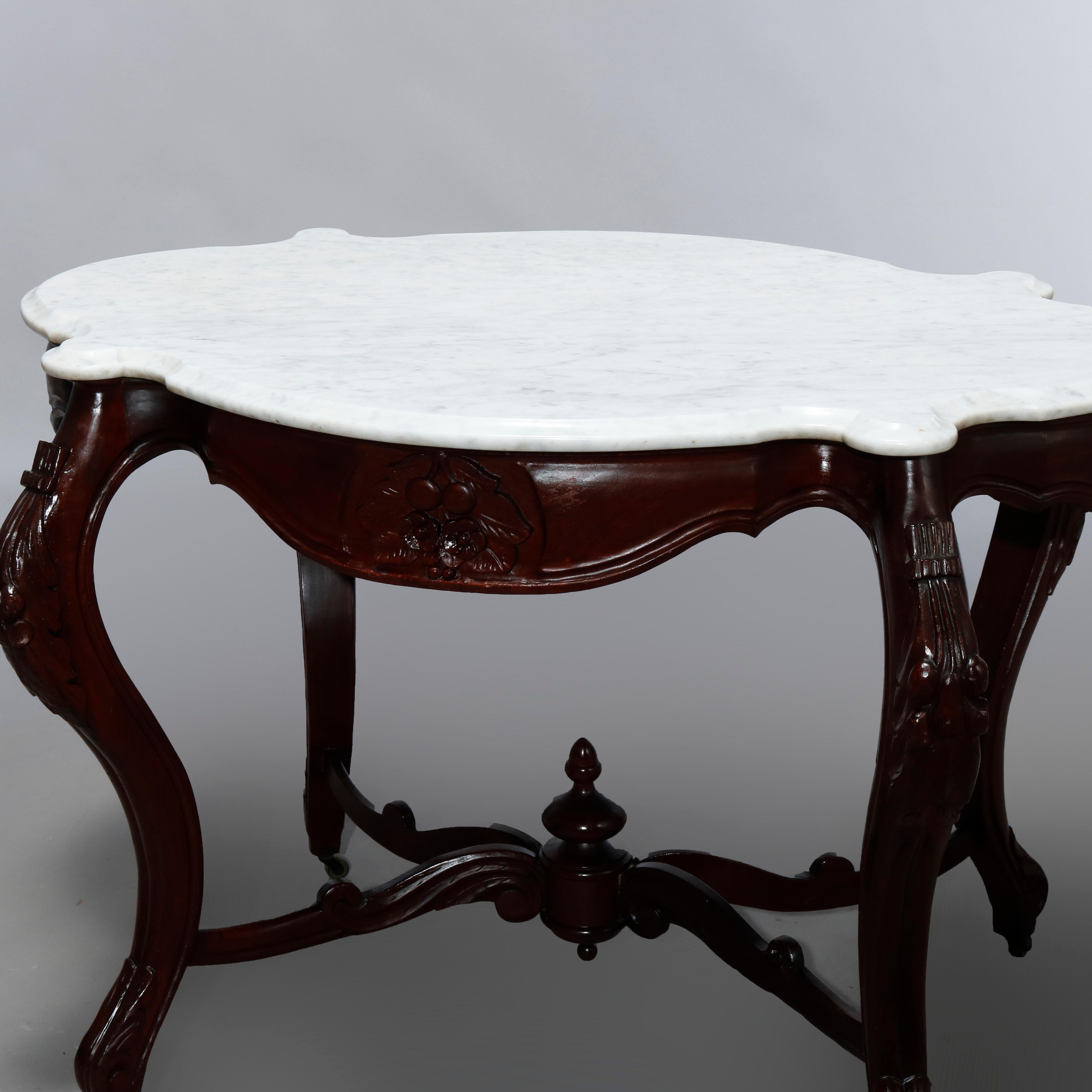 An antique Rococo Revival turtle top center table offers shaped marble top over walnut base having skirt with carved fruit and foliate reserve and raised on cabriole legs with scroll form stretcher and center urn finial, c1870

Measures: 29.75