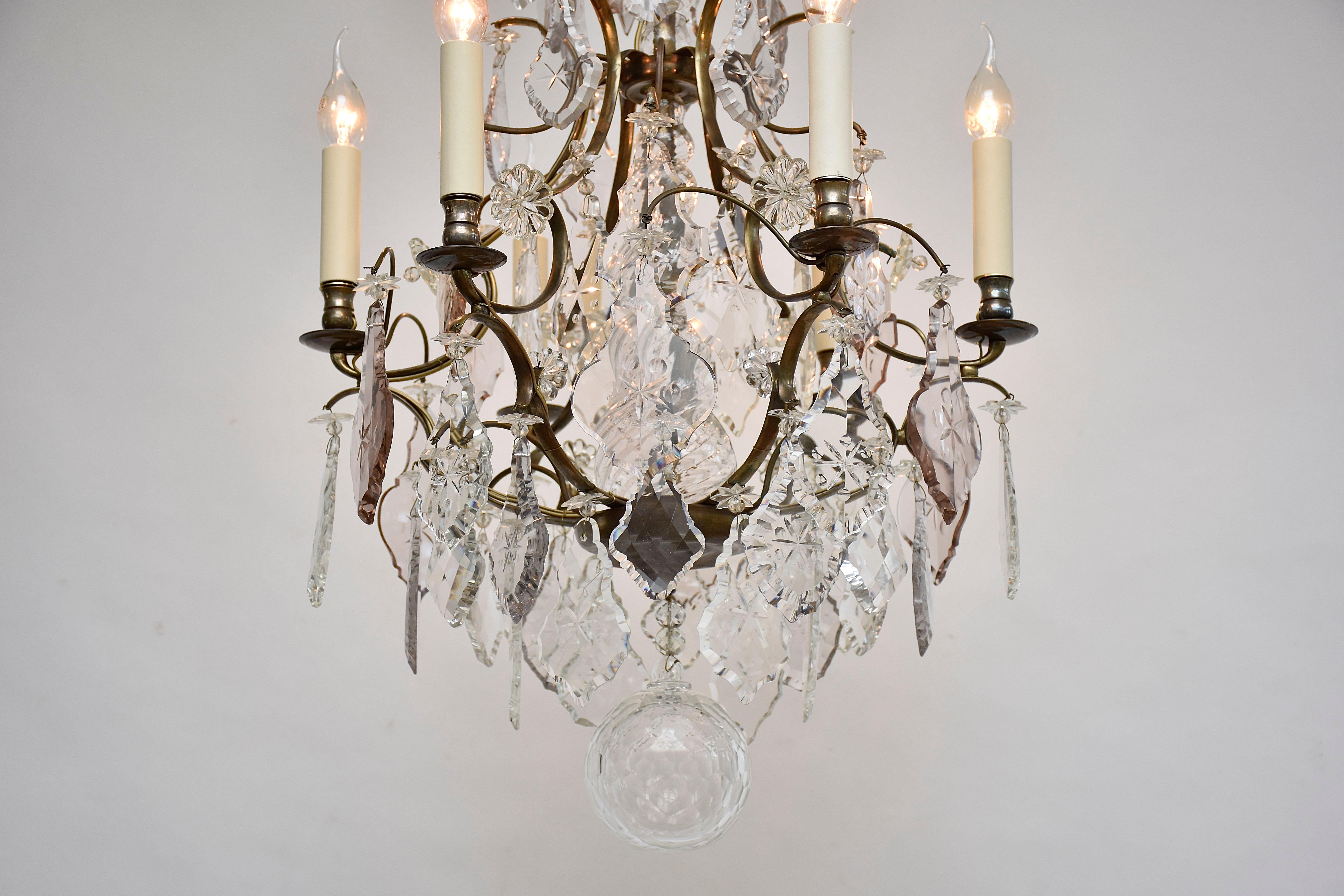 Un bellissimo lampadario in stile rococò a 6 luci.
Il lampadario è riccamente decorato con  bellissimi pendenti in cristallo tagliato di grandi dimensioni, rosette di fiori e stelle. Alcuni cristalli sono di colore tenue.
Il gambo centrale è coperto