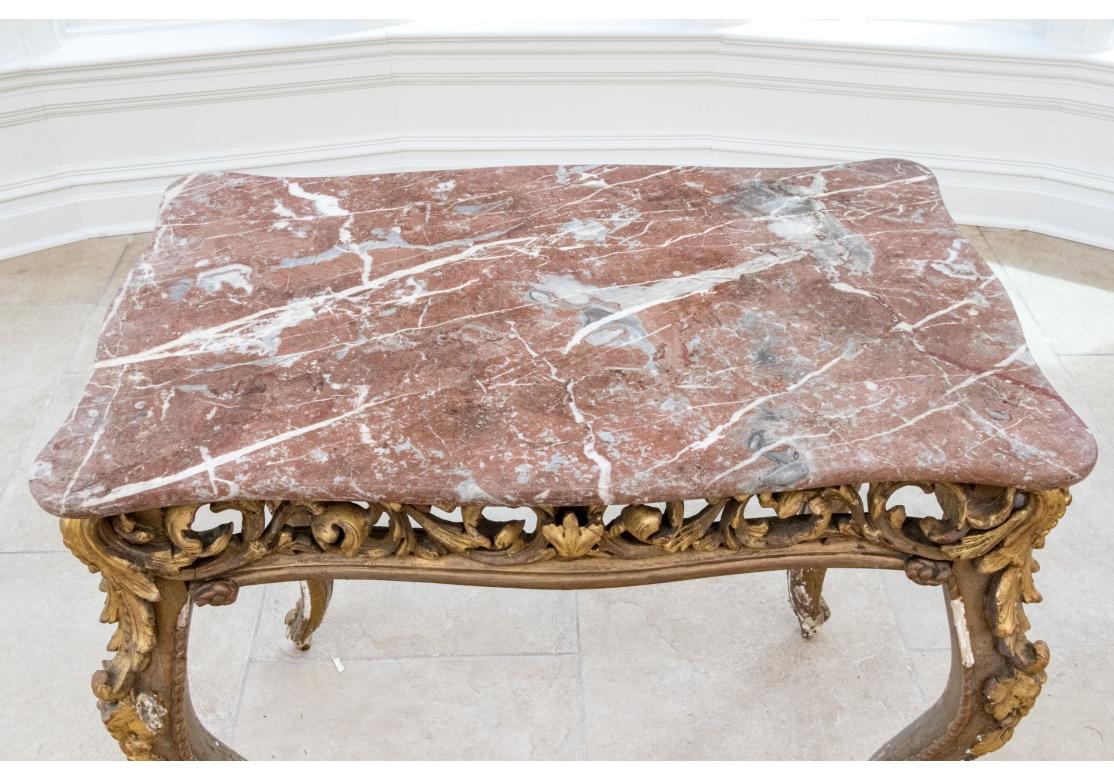 An elegant Antique French Gilt wood Parlor Table with  extensive carving and fine striated Rose Marble Top. The table with pronounced Cabriolet legs and fine pierced and carved open apron with strongly carved Acanthus leaf accents. . Restoration is