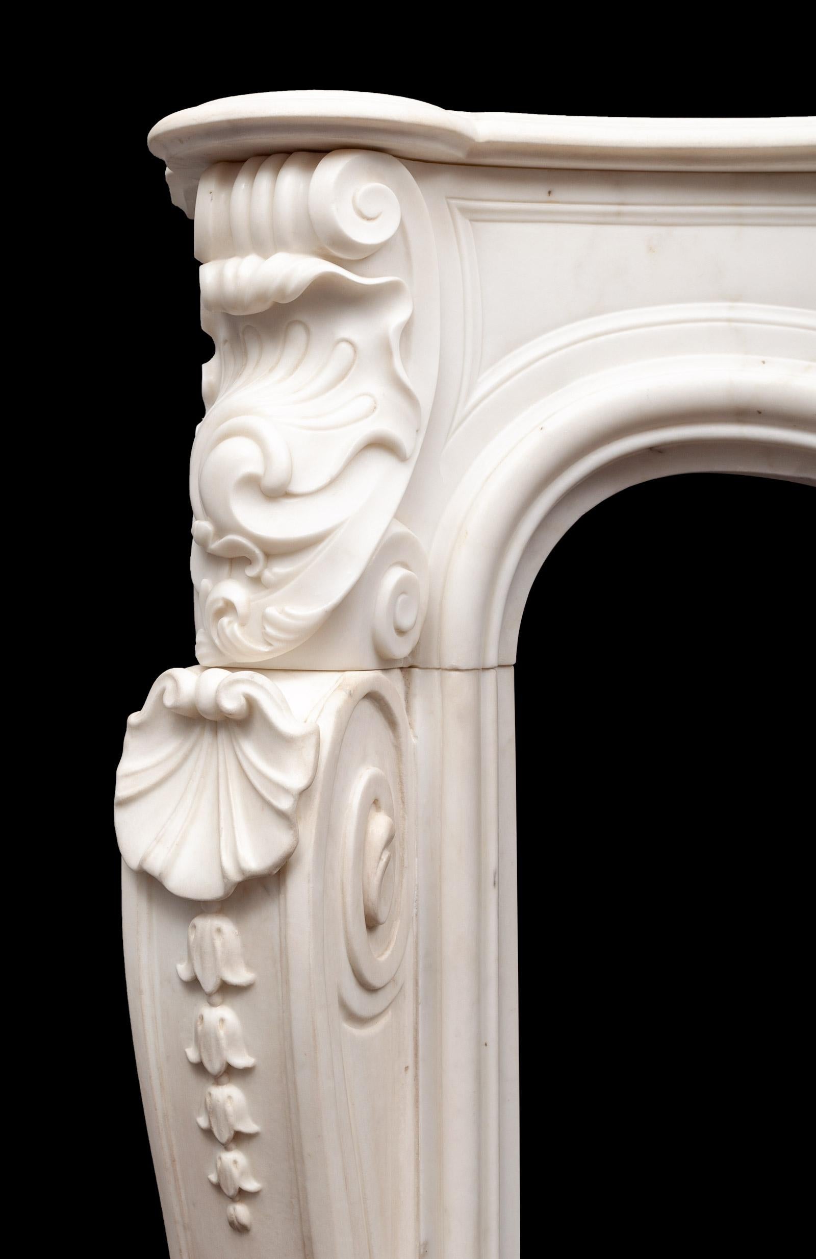 An antique Rococo style statuary marble fireplace surround of great quality, proportions and scale. Beautifully carved in the finest and purest white statuary marble.

The serpentine shaped and moulded shelf above a frieze centred by a stylized