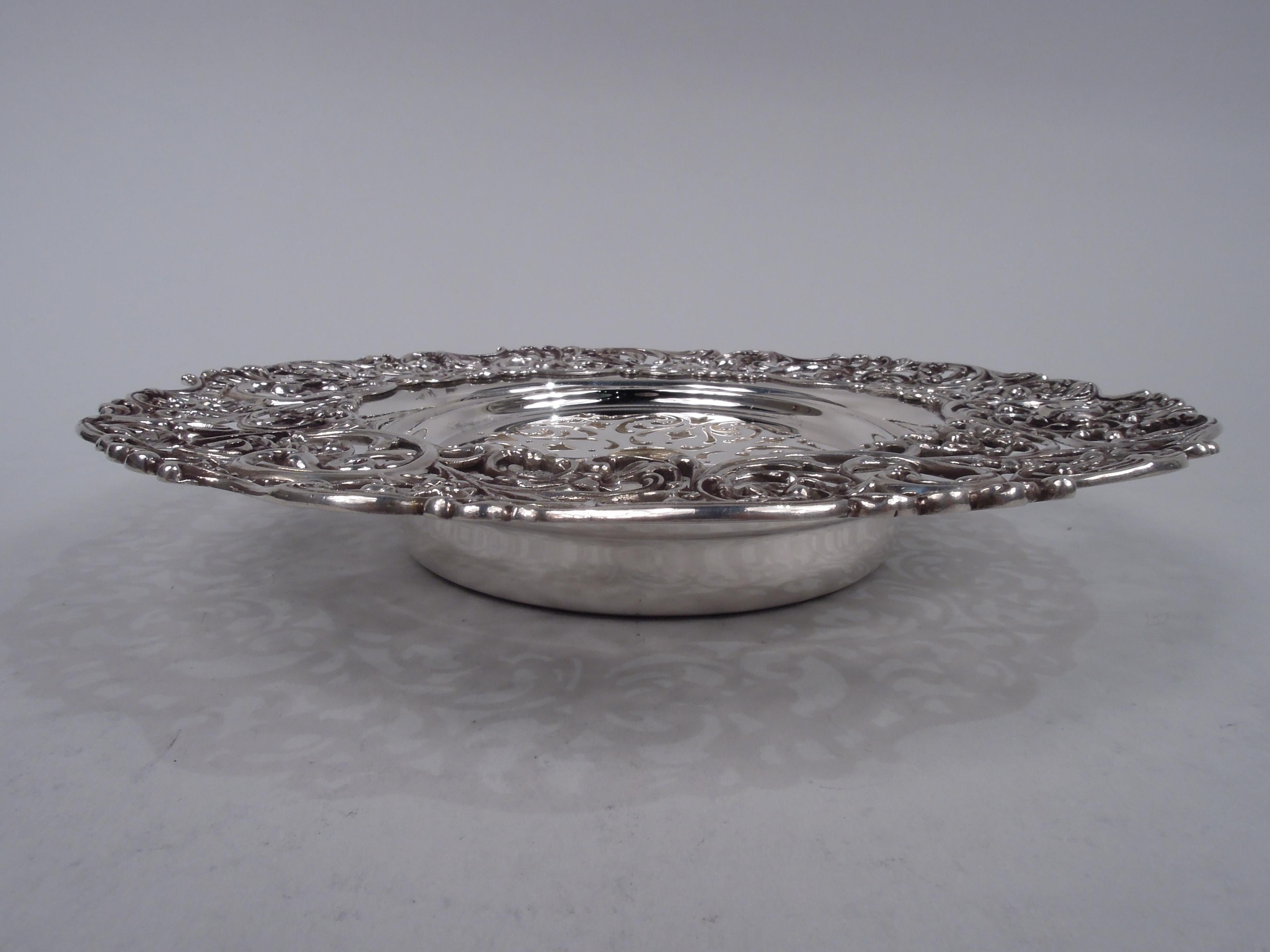 Edwardian sterling silver butter dish, ca 1900. Round and deep well. Applied wide and cast rim with open leafing scrollwork and flowers. Liner has ornamental piercing. Fully marked including stamp for Roger Williams, a Providence maker that merged
