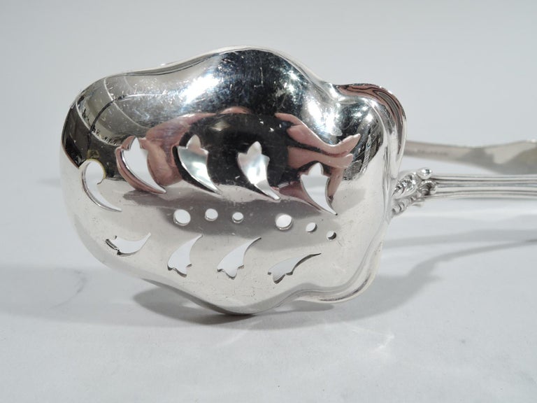 Corinthian sterling silver ice tongs. Made Roger Williams in Providence. U-form with pierced jaws. Terminals have fluid shell and leaf ornament. Roger Williams was active in the early 1900s. It merged with Mauser in 1903 to form the Mt Vernon