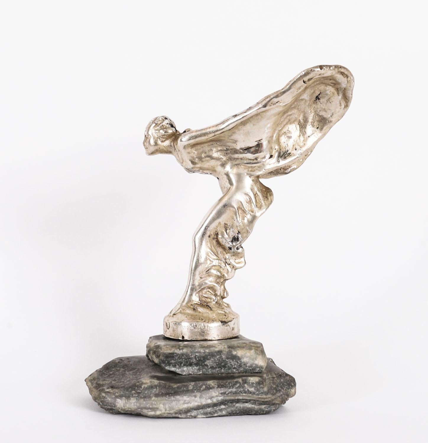 An early 20th century Spirit of Ecstasy designed by Charles Sykes, incised Charles Sykesl R.R Ltd 6.2.11 to the base, mounted to a gray rocky marble plinth base, Circa 1924 in date.

The numbers engraved on the base, 