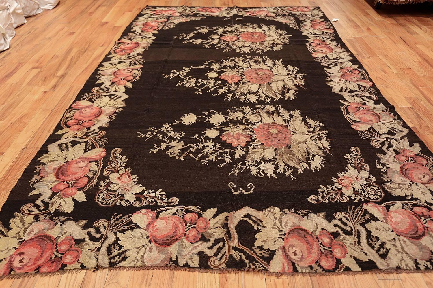 Three perfectly stitched bouquets are splayed across the center of this antique Bessarabian rug, each displaying floral red roses, detailed with shaded petals and surrounded by desaturated yellow and green leaves. The light colors are set off