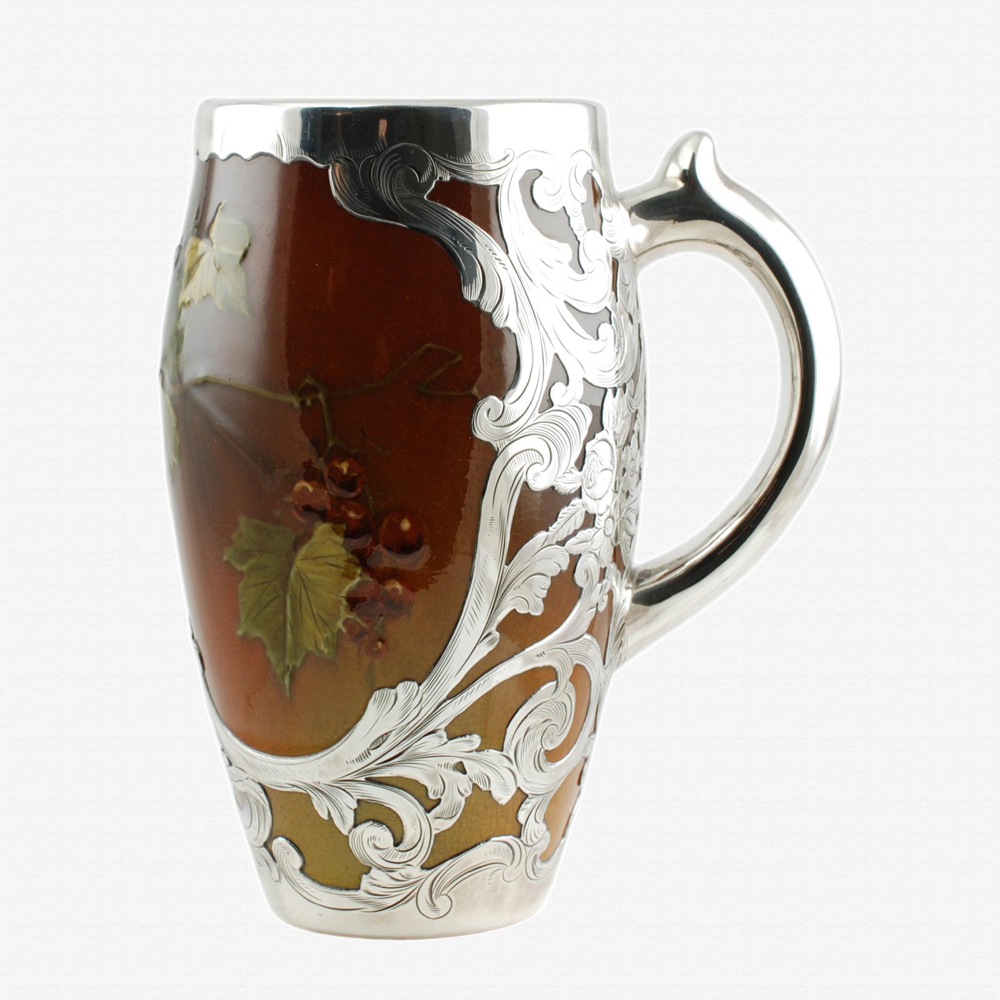 This late 19th century glazed earthenware mug was crafted in the studios of Cincinnati Ohio's renowned Rookwood Pottery Company and has a traditional form with an ear-shaped handle having a thumb rest. The exterior of the piece is finished in