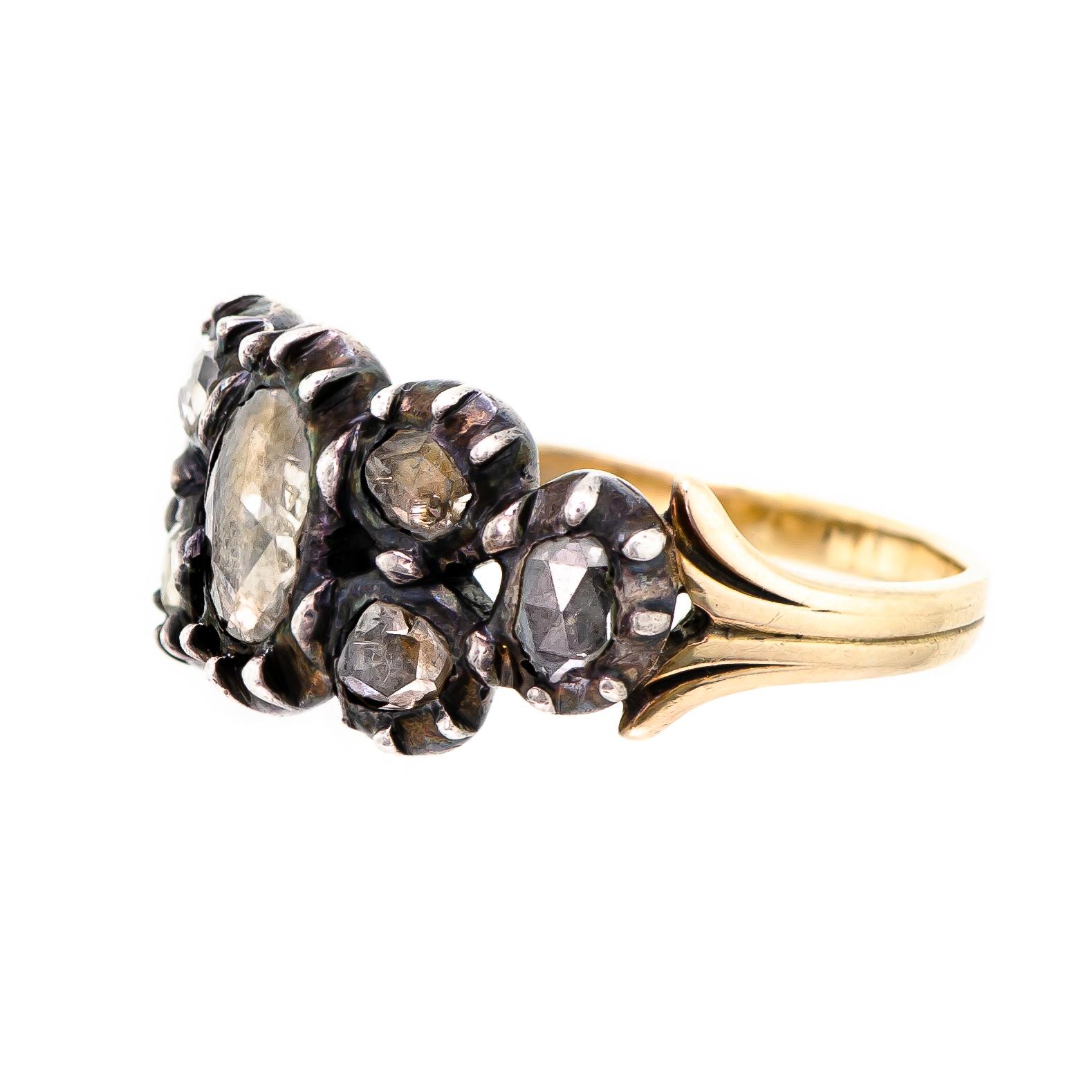 This alluring antique late Georgian early Victorian diamond ring is handcrafted in silver over yellow gold. Set with seven (7) crimped collet and prong closed-back majestic rose-cut diamonds of varying sizes. These beautiful diamonds are foil-backed