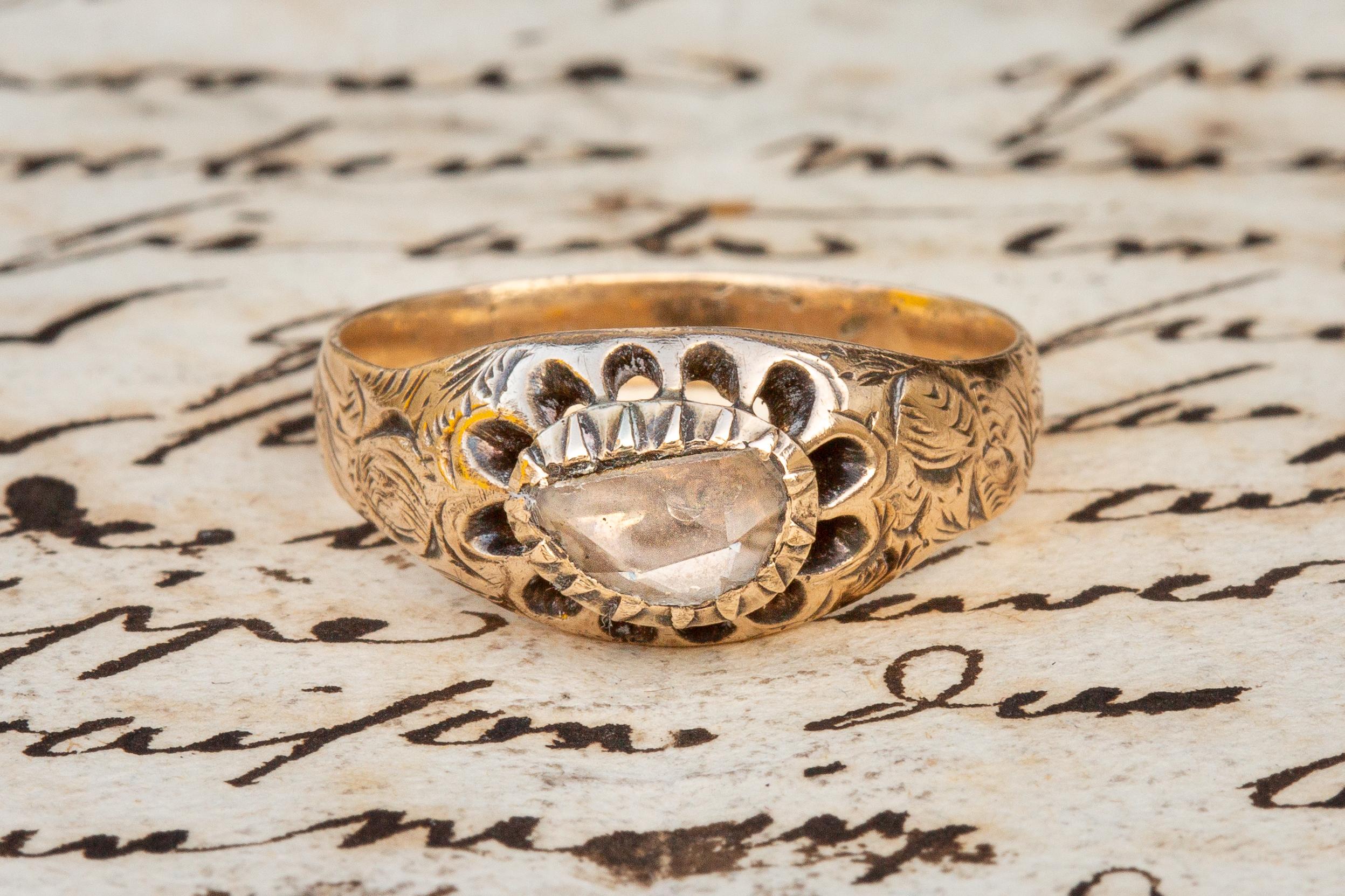 This beautiful piece was made in France and dates to the early 19th century. The ring is set with an oval rose cut diamond in a cut down rub over setting. The closed back diamond rests in a ‘belcher’ setting with 12 u-shaped curves to create a petal